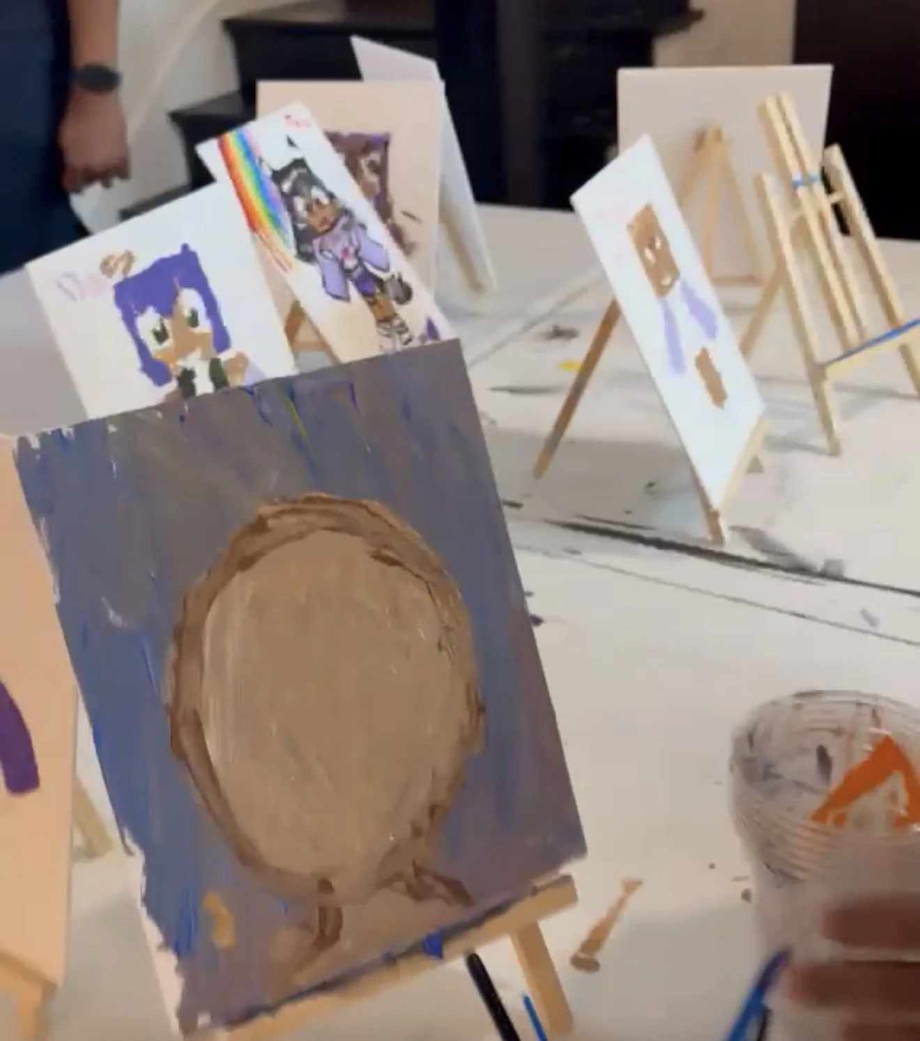 Paintings on easels displaying various artwork including cartoon characters and abstract designs inside an art studio.