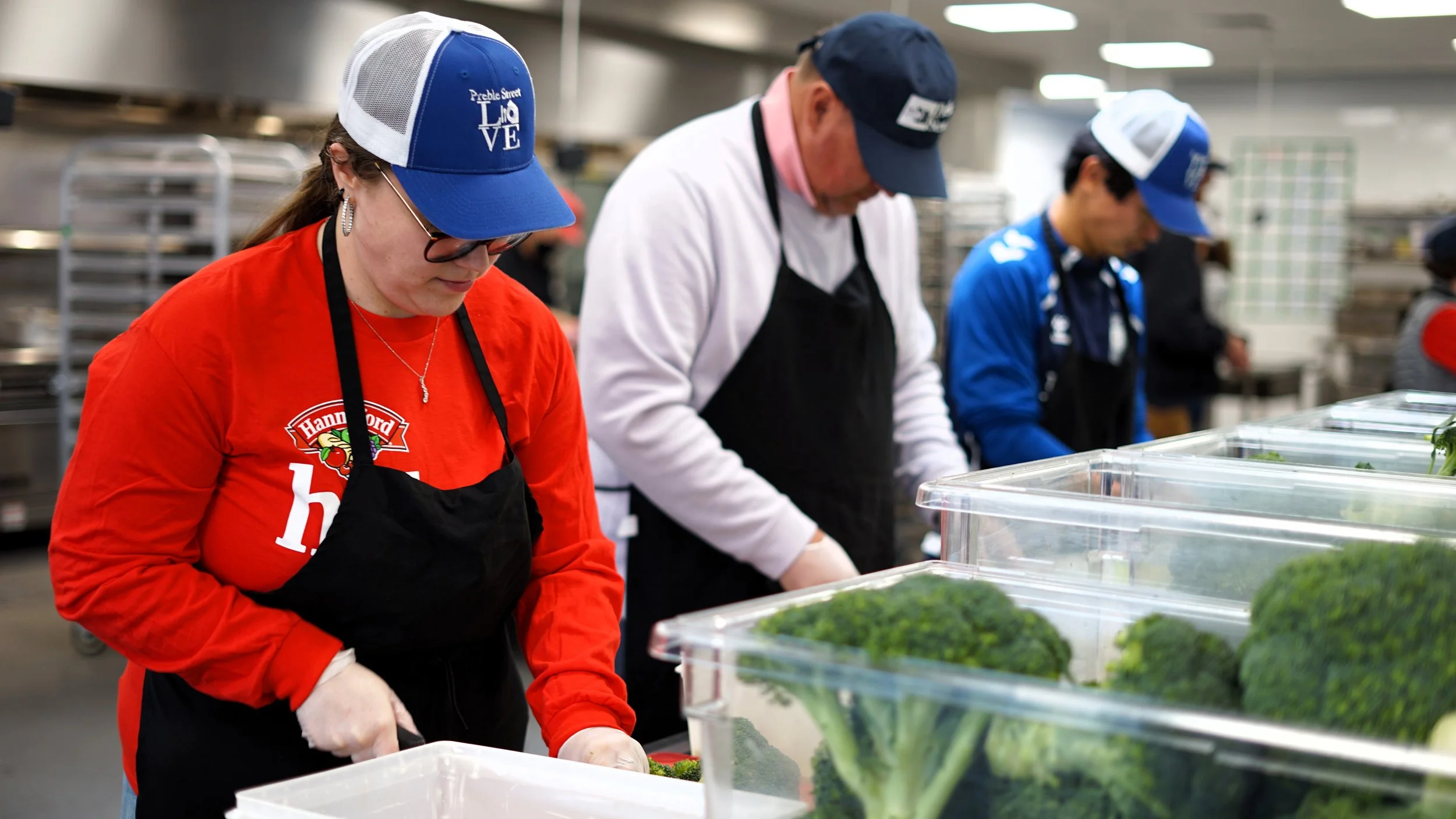 People working in a food packaging facility, sorting leafy greens in clear plastic containers.
