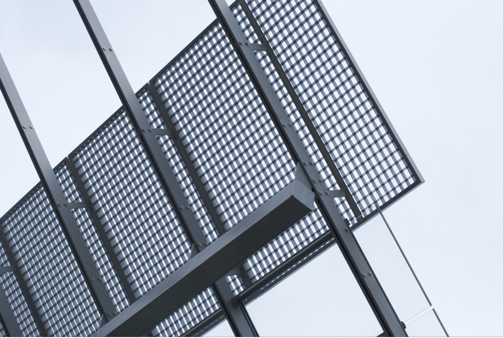 Close-up of a black metal fire escape with a grid design against a light gray sky