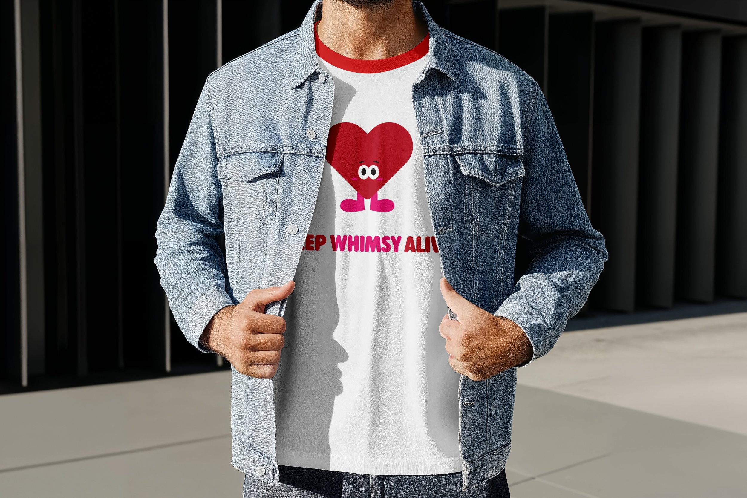 A person wearing a light blue denim jacket over a white t-shirt with a graphic of a red heart with eyes and pink legs, and the text "Keep Whimsy Alive" in pink. The person is standing outdoors in front of a black fence with vertical bars and a modern