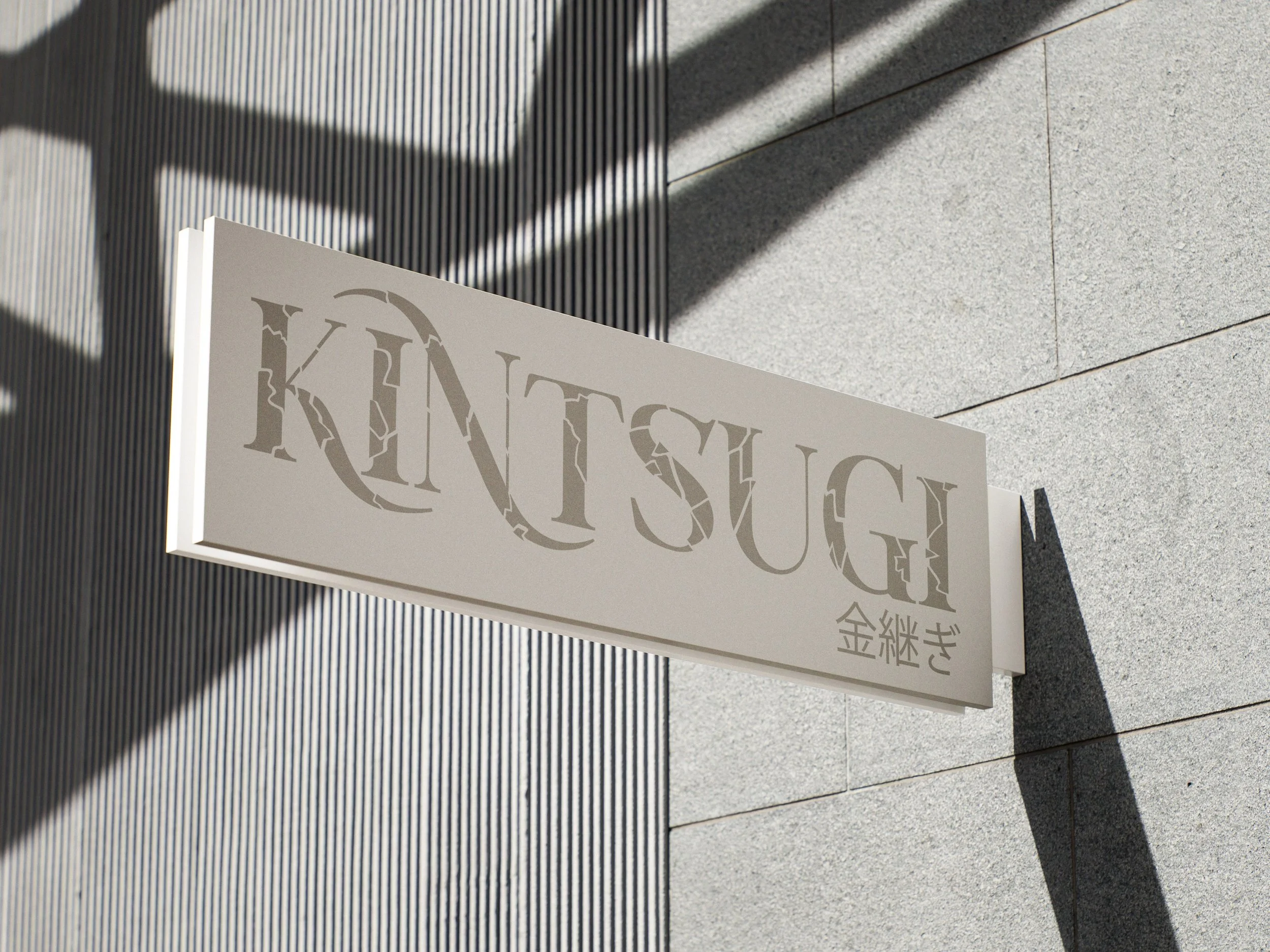 Close-up of a sign with the word 'KINTSUGI' in stylized letters, mounted on a wall with shadows cast on the surface.