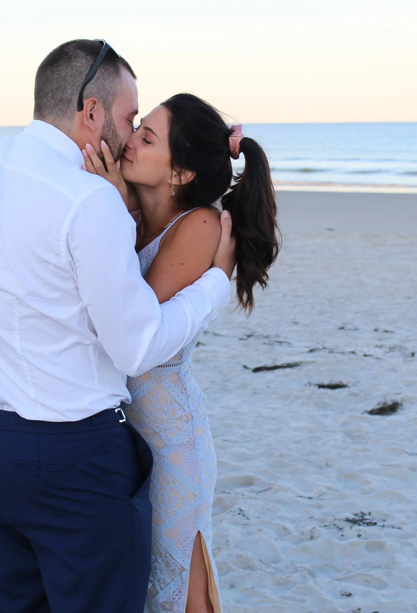 A couple sharing a kiss on the beach during sunset, with the ocean in the background.