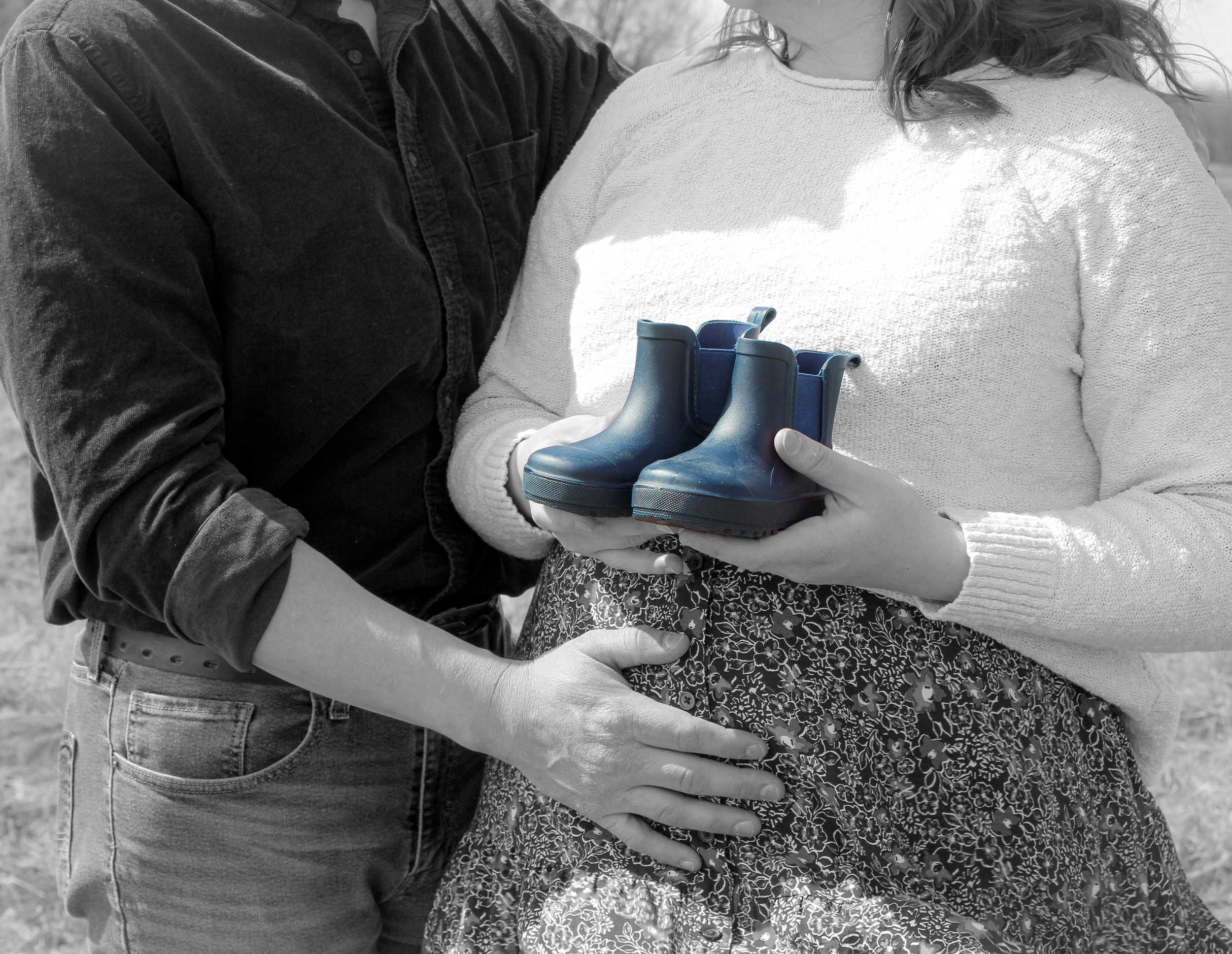 A person holding a pair of miniature blue rain boots, with another person standing close by outdoors.