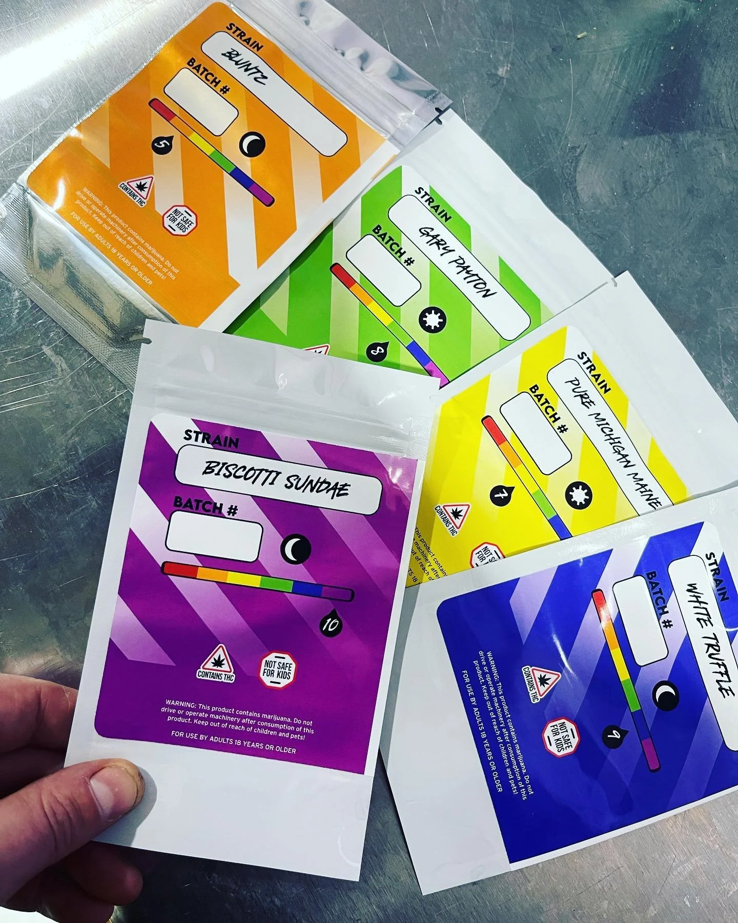 Colorful drug test result cards with strain names and color-coded THC levels, in orange, green, purple, and blue, on a metallic surface.
