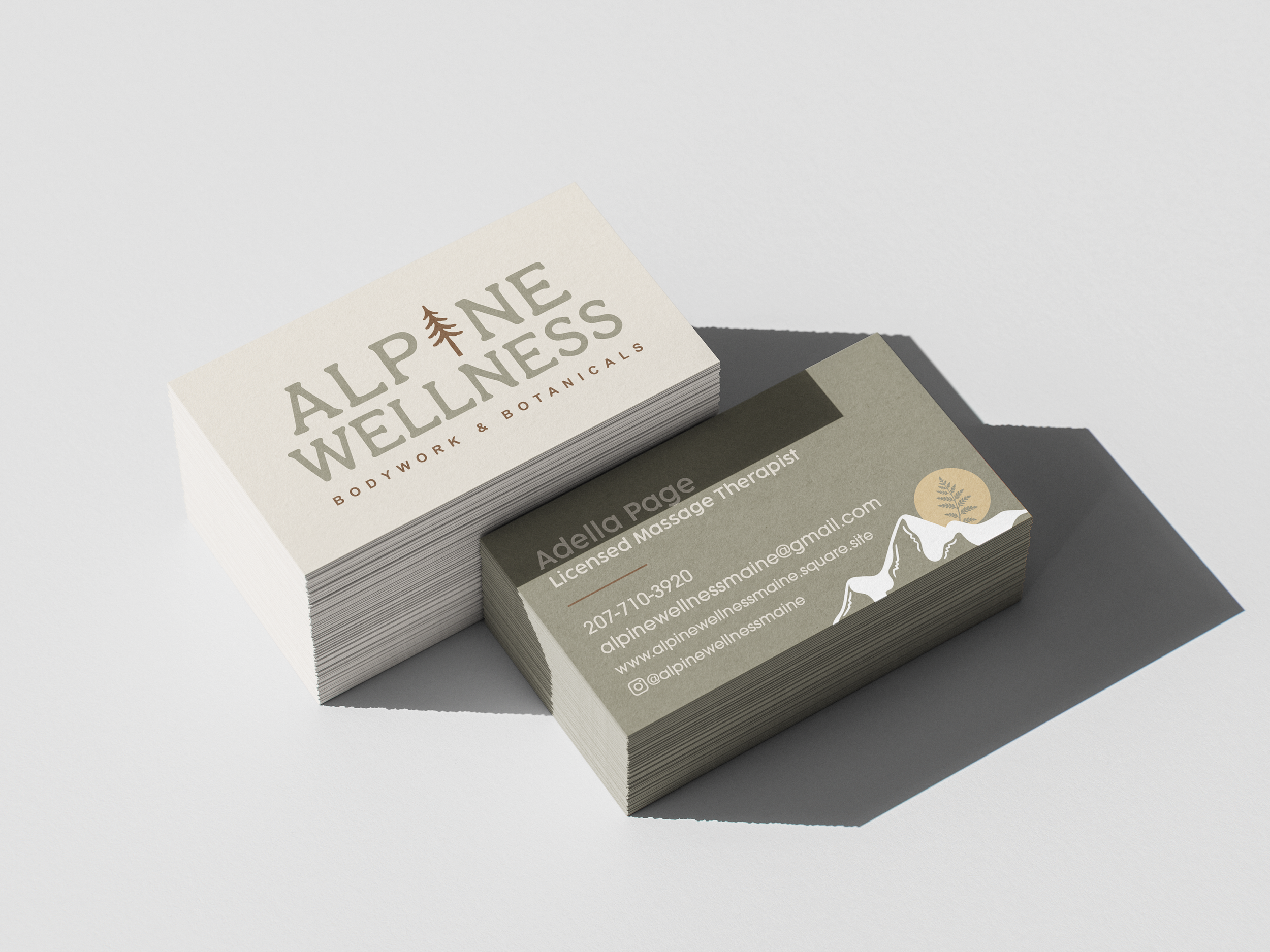 A stack of business cards for Alpine Wellness, a bodywork and massage therapy business, placed on a flat surface with a shadow cast on the background.