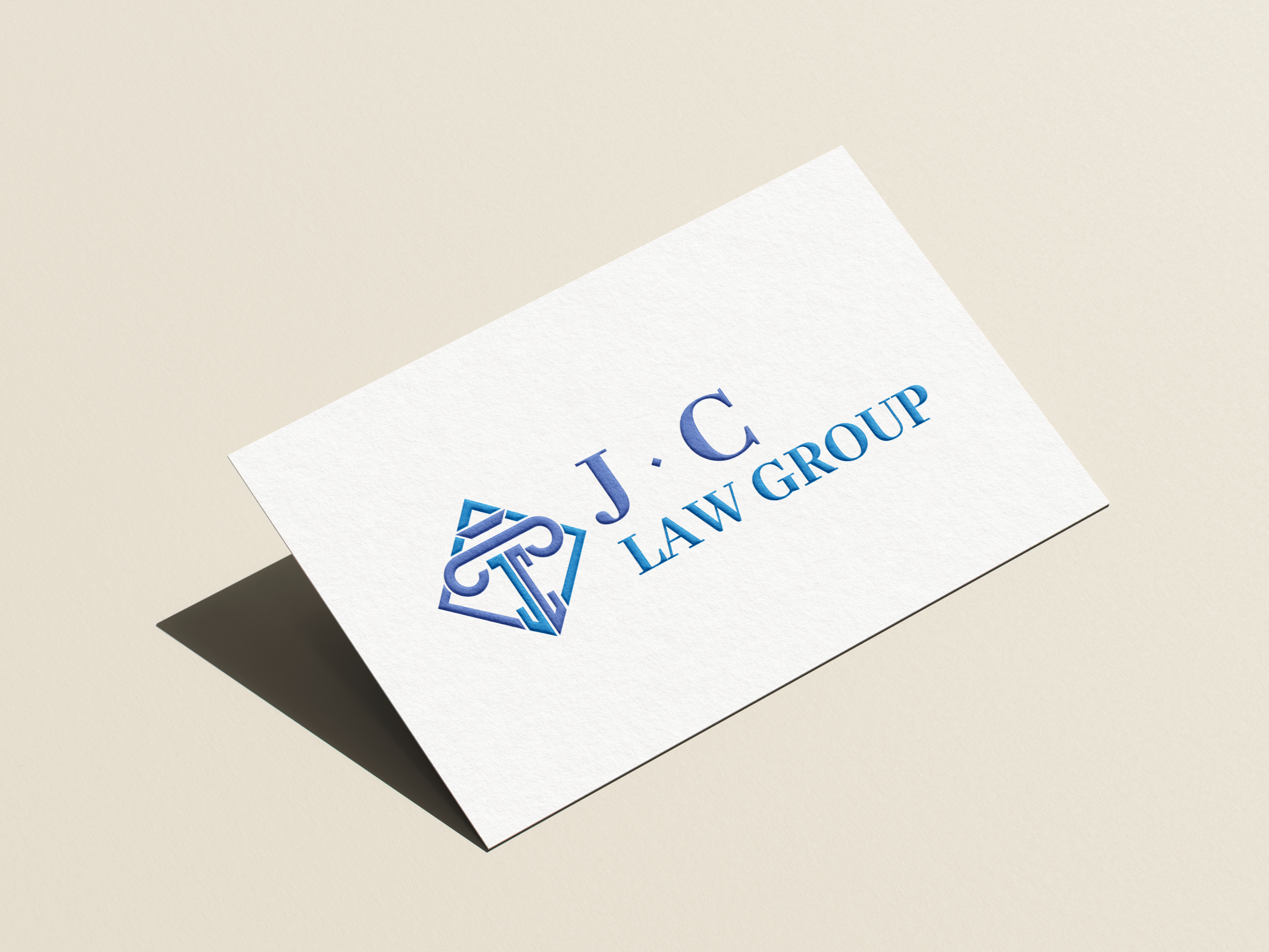 Close-up of a business card with the initials 'J.C.', the words 'LAW GROUP', and a blue geometric logo, resting on a white surface.