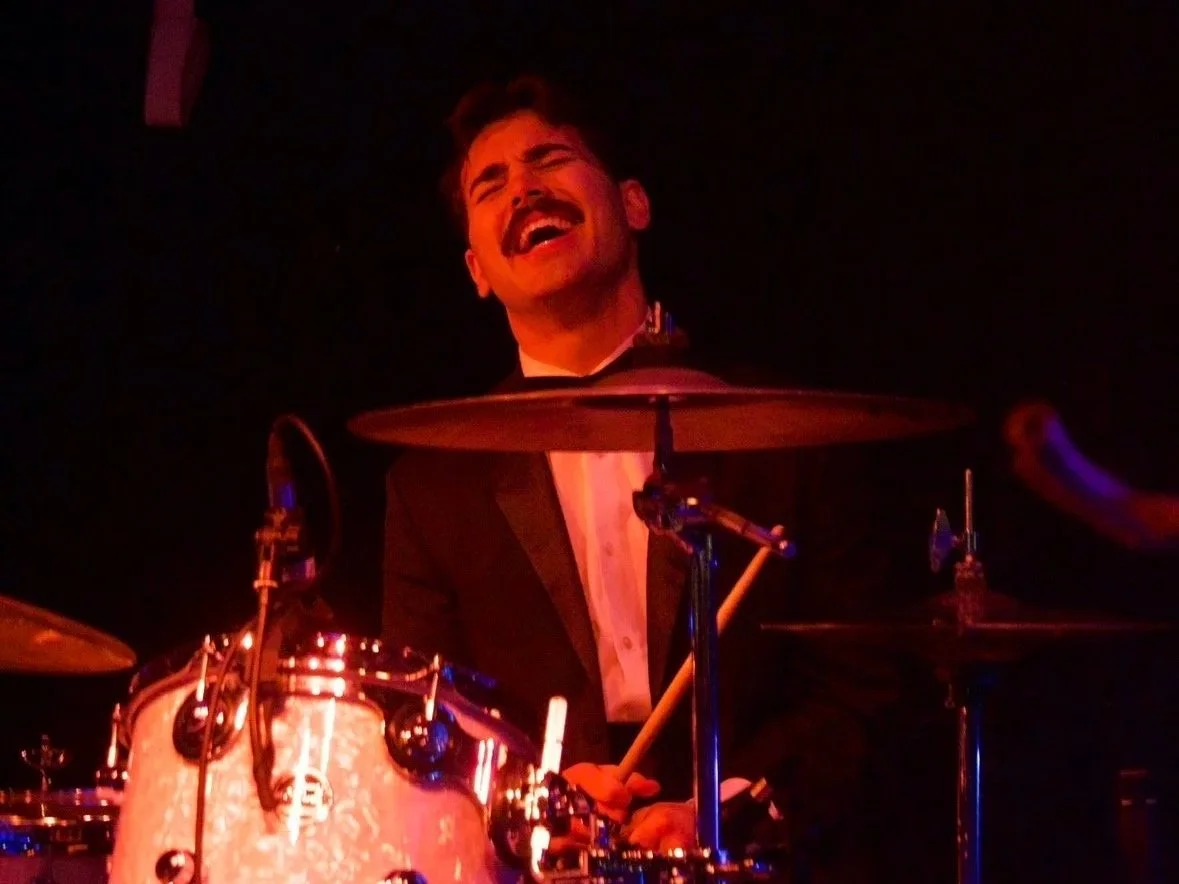 A man playing drums on stage, laughing.