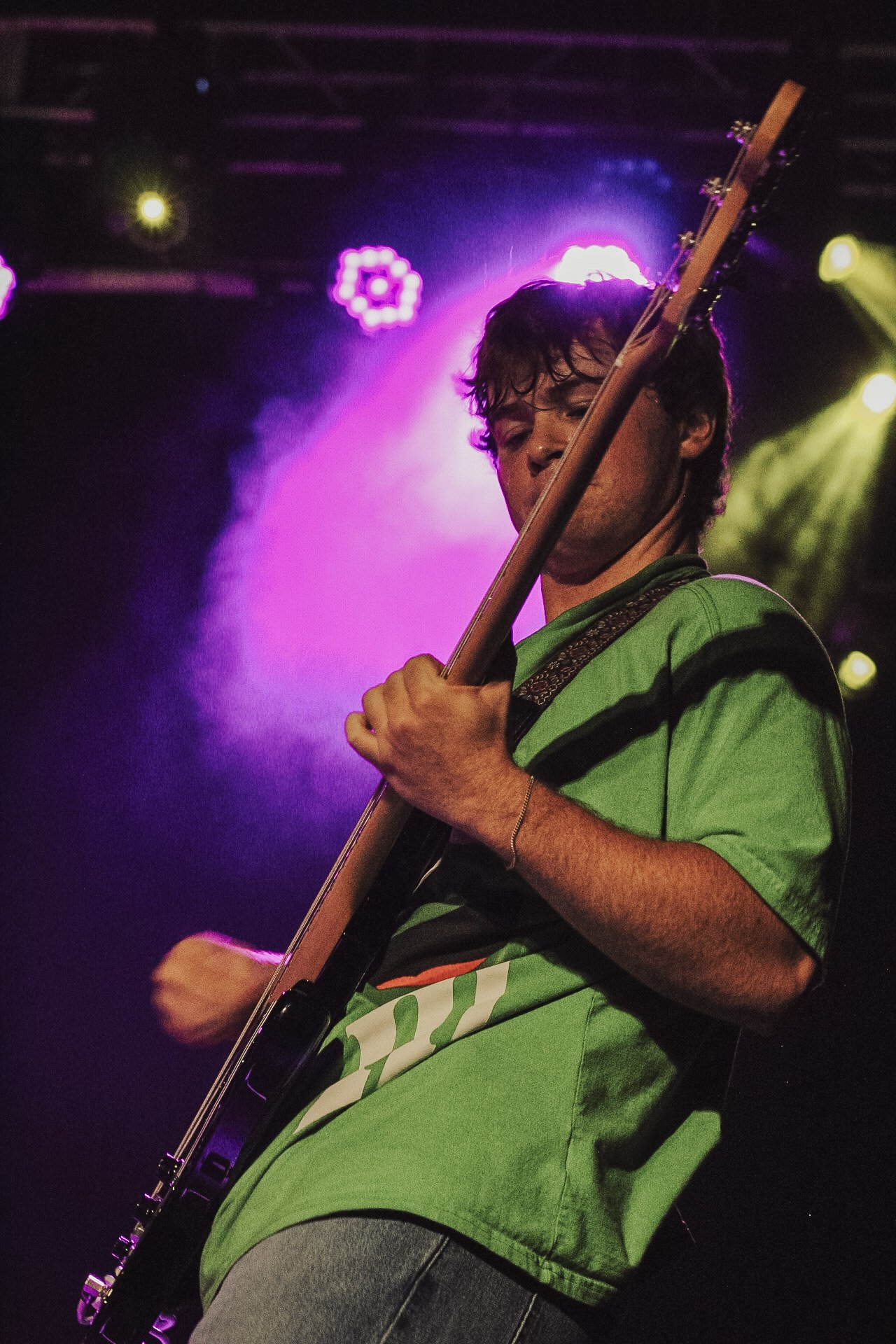 Young male musician playing an electric guitar on stage with colorful stage lights behind him.