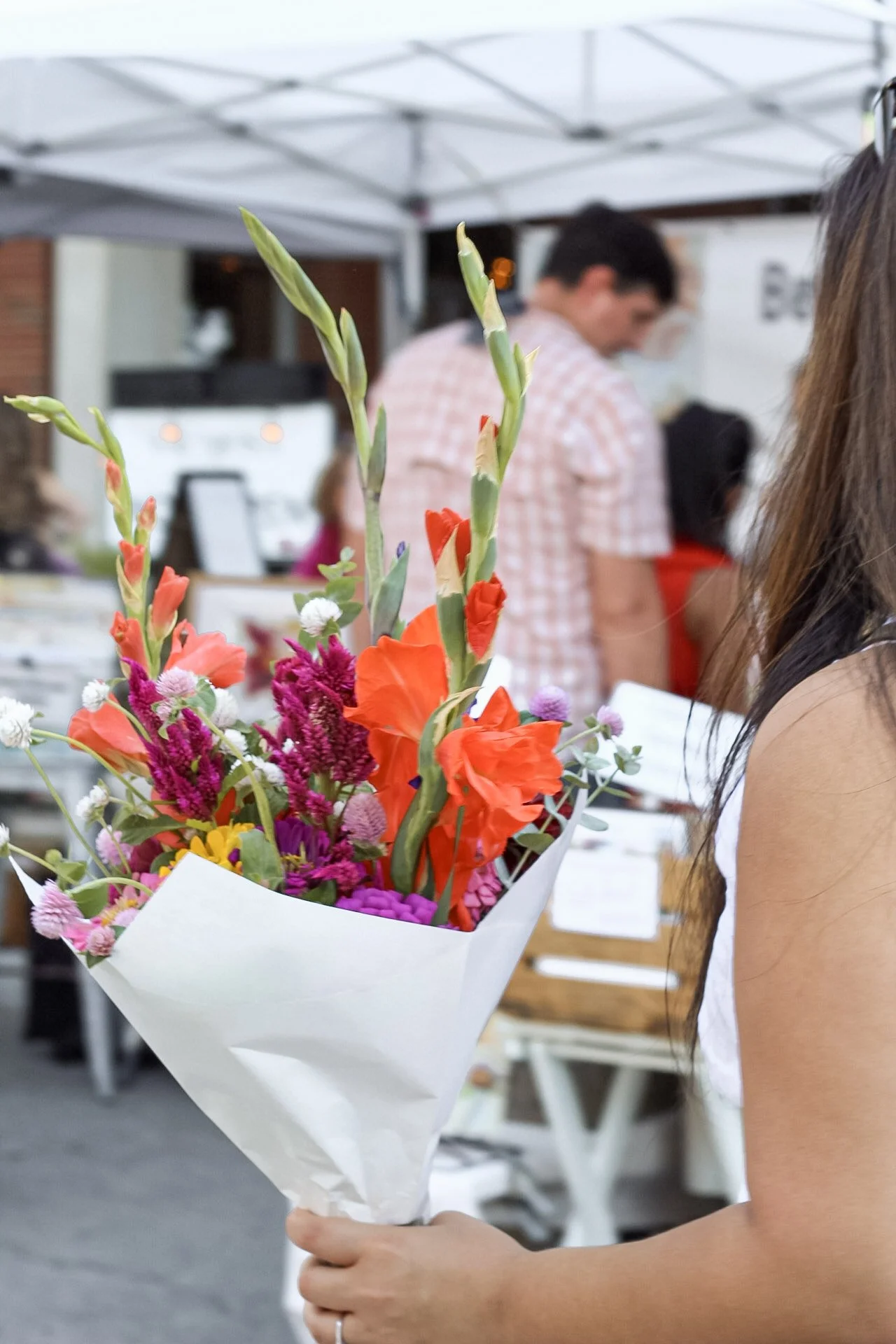 Person holding a bouquet of colorful flowers at an outdoor event or market.