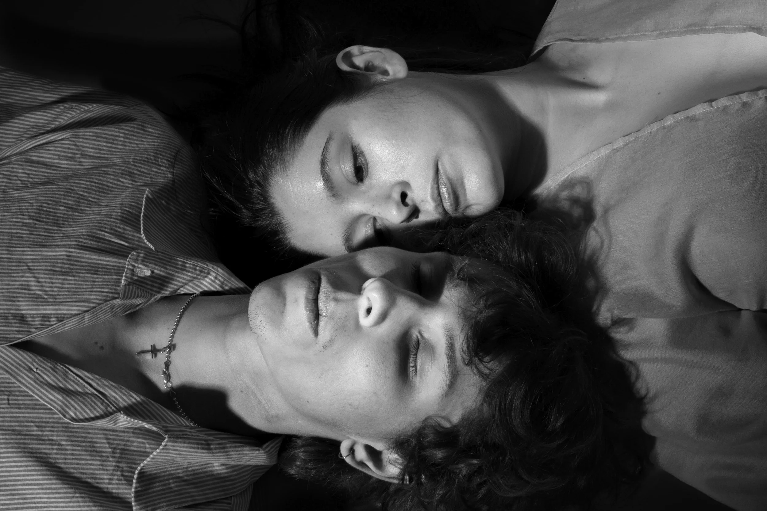 Two people lying close together with eyes closed, appearing to be resting or sleeping. The photo is in black and white.