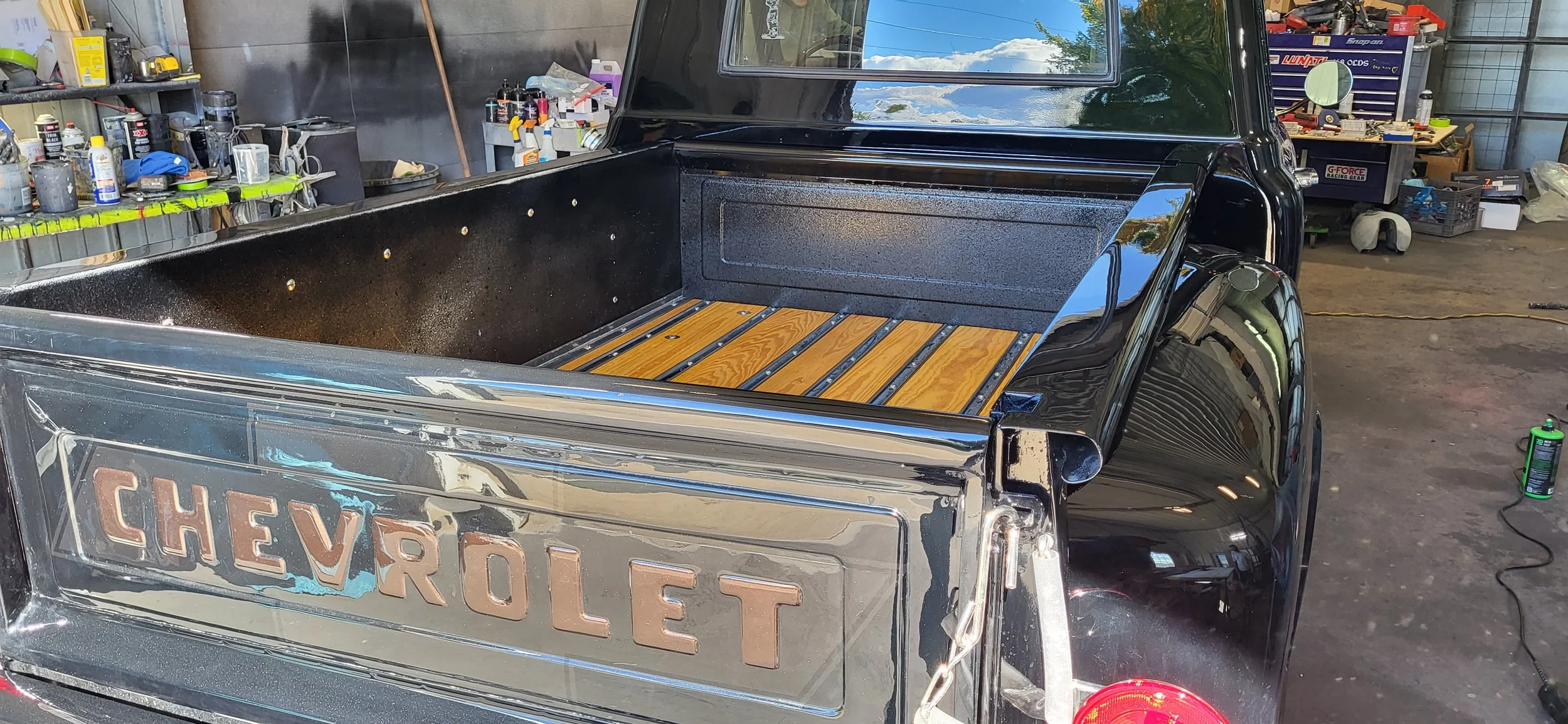 Restored black Chevrolet pickup truck with polished chrome trim and wood-plank bed inside an automotive workshop