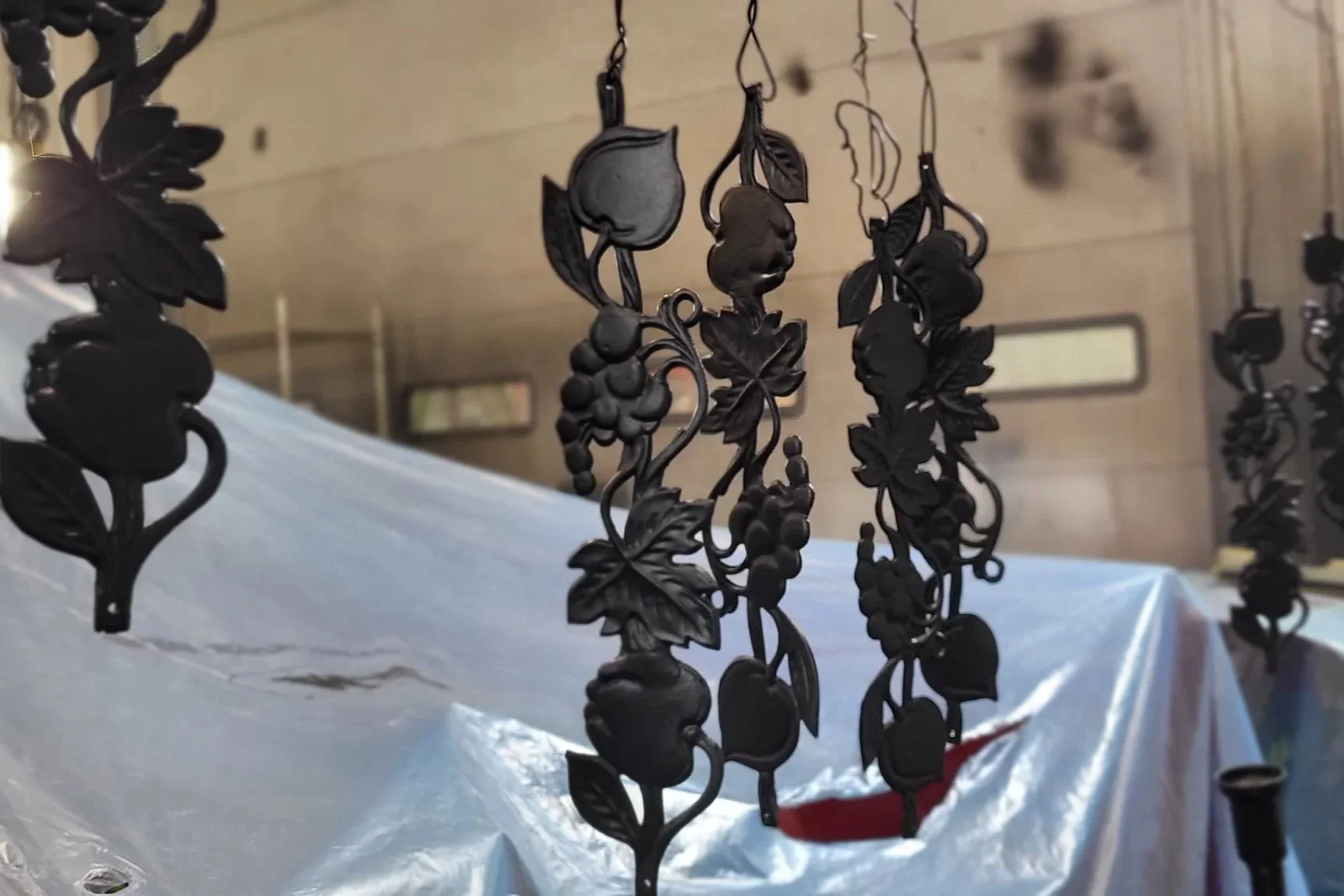 Black metal grapevine and fruit ornaments hanging above a table covered with white plastic.