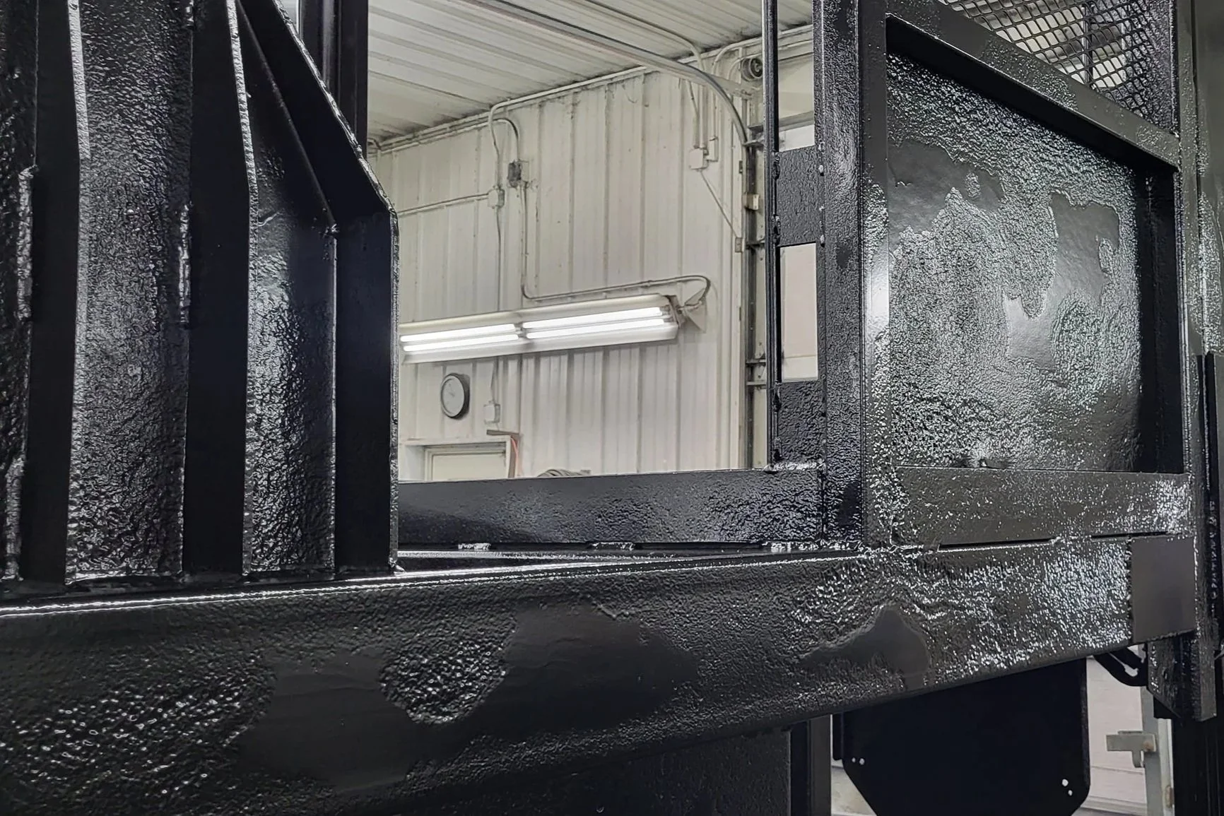 Black industrial metal enclosure with an open access panel in a fluorescent-lit workshop