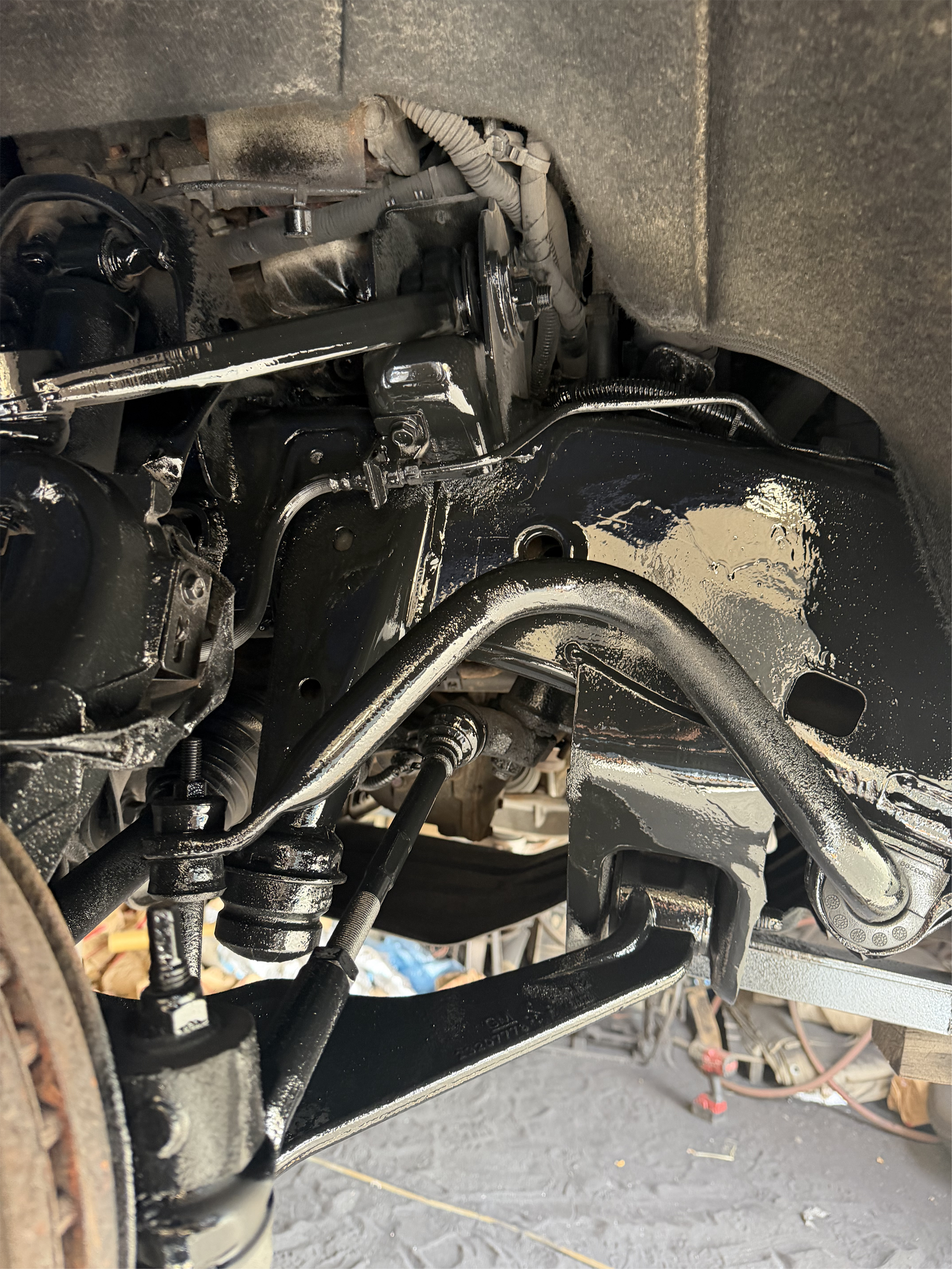 Close-up of a vehicle’s freshly painted black front suspension, steering linkage, control arms, and brake components.