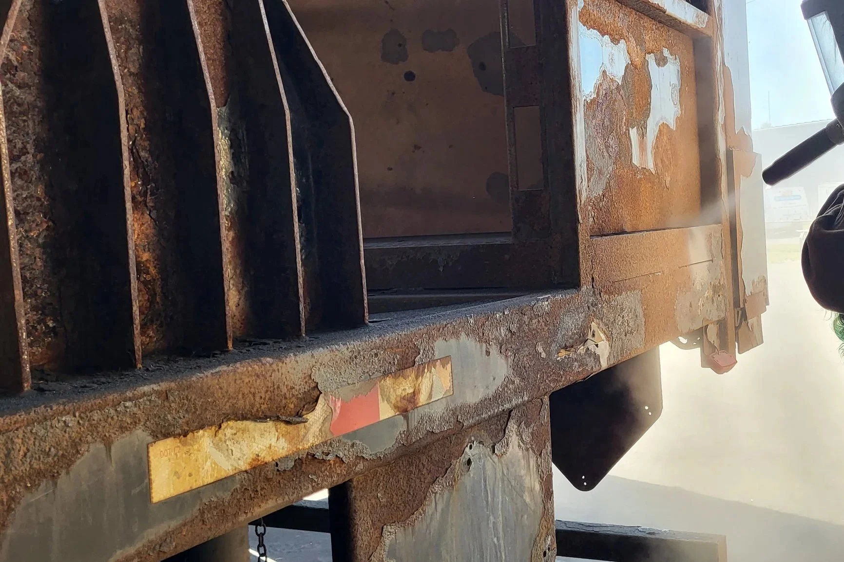 Close-up of a rusted industrial metal structure with peeling paint, vertical supports, and a partially visible person beside it