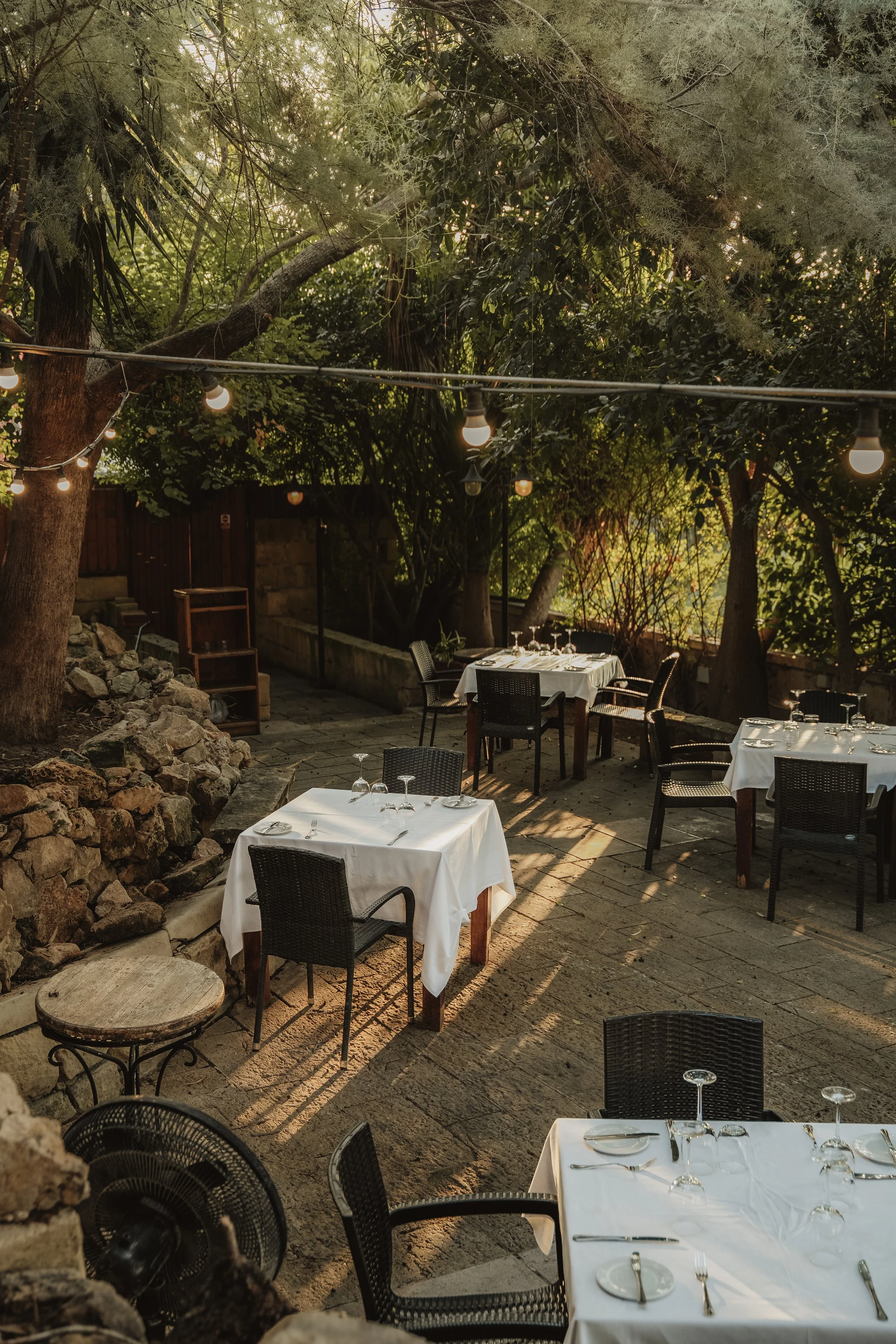 Outdoor restaurant terrace with set tables under trees, venue photography Malta