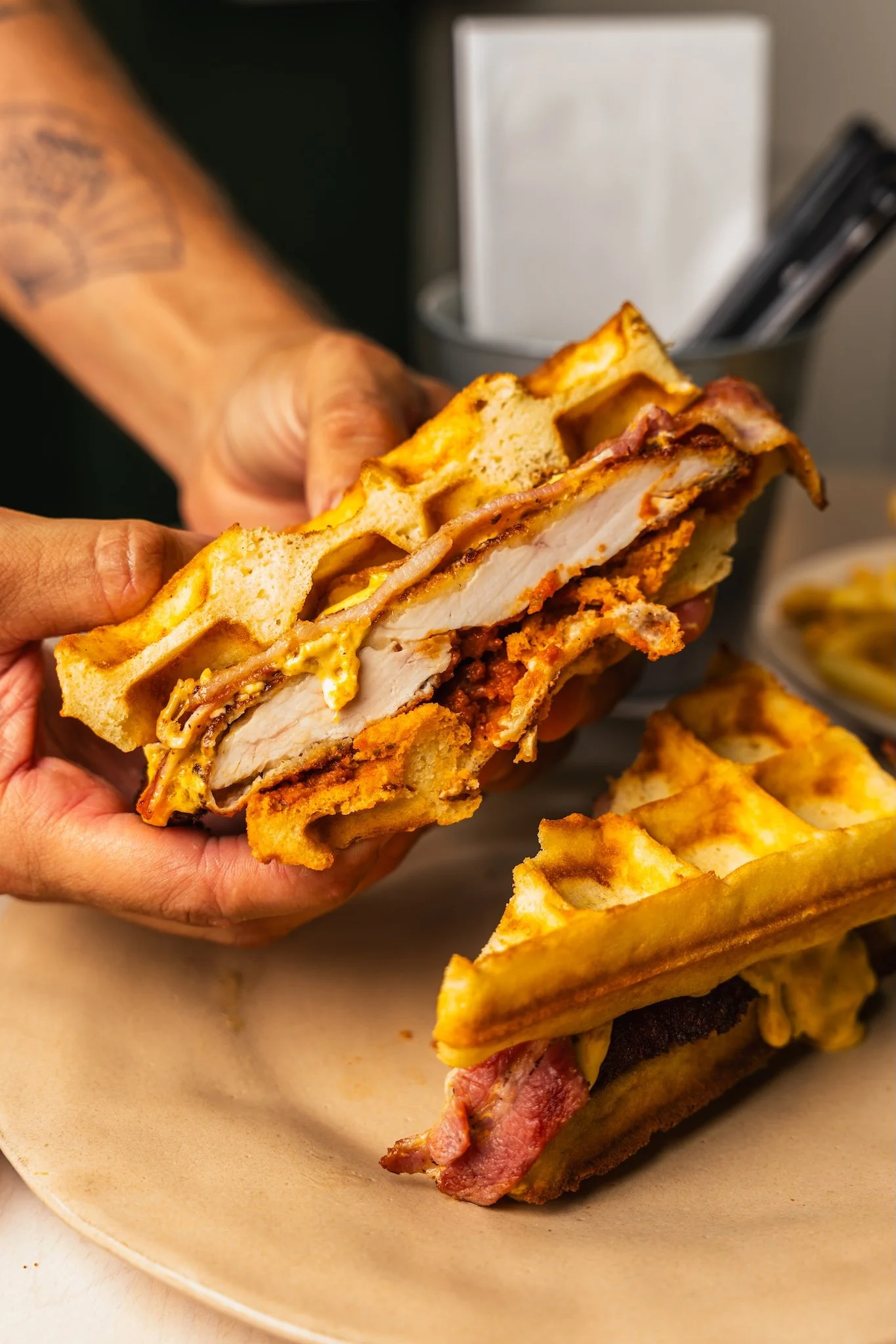 Hands holding a fried chicken waffle sandwich, restaurant food photography