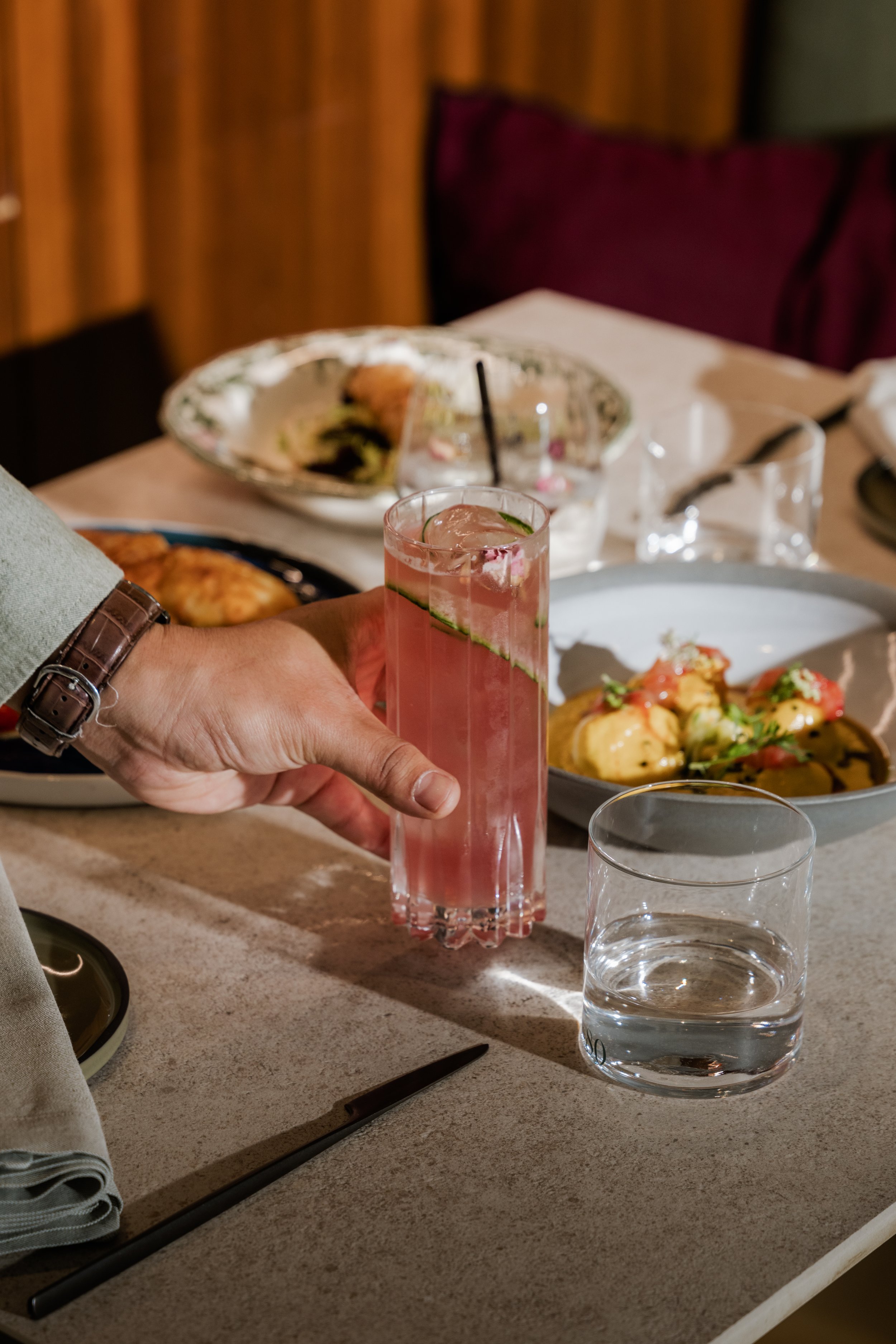 Hand holding a pink cocktail at a restaurant table, drinks photography Malta