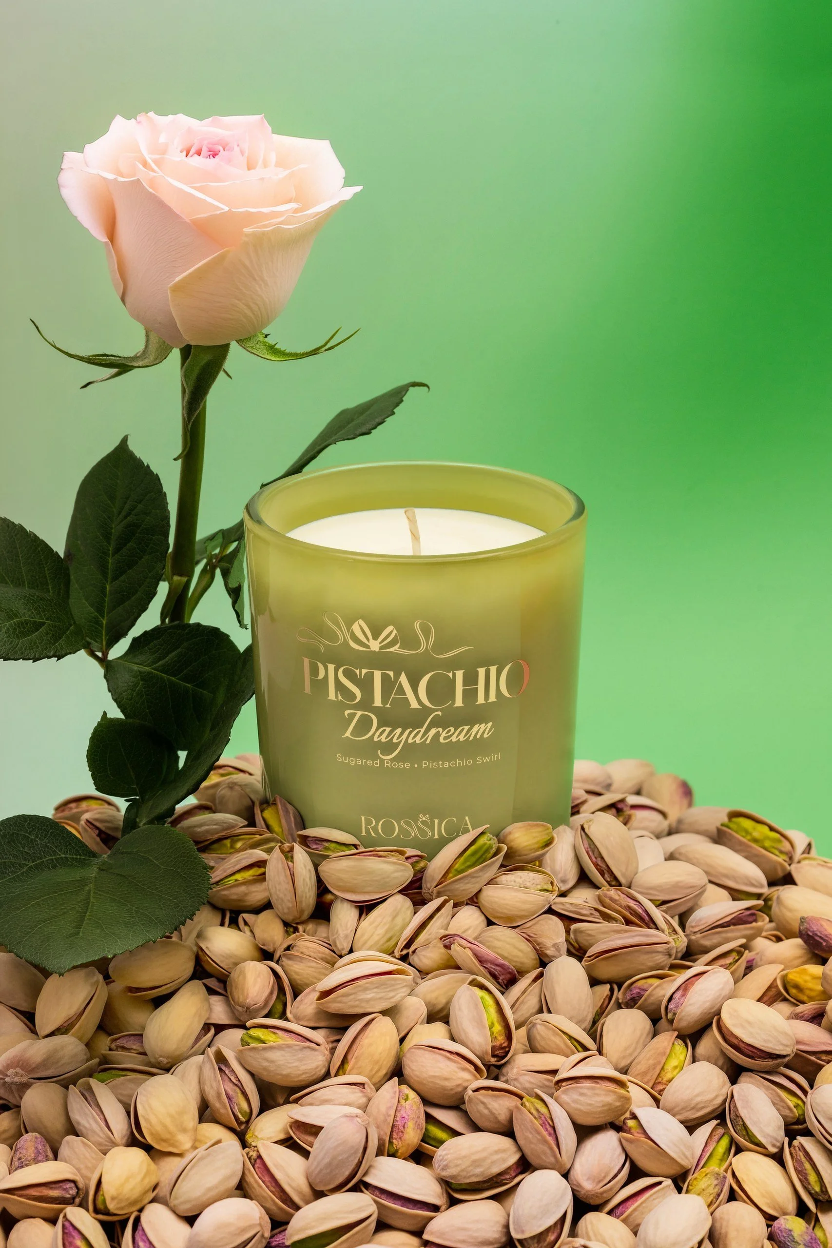 Pistachio scented candle with a pink rose on a bed of pistachios, product photography