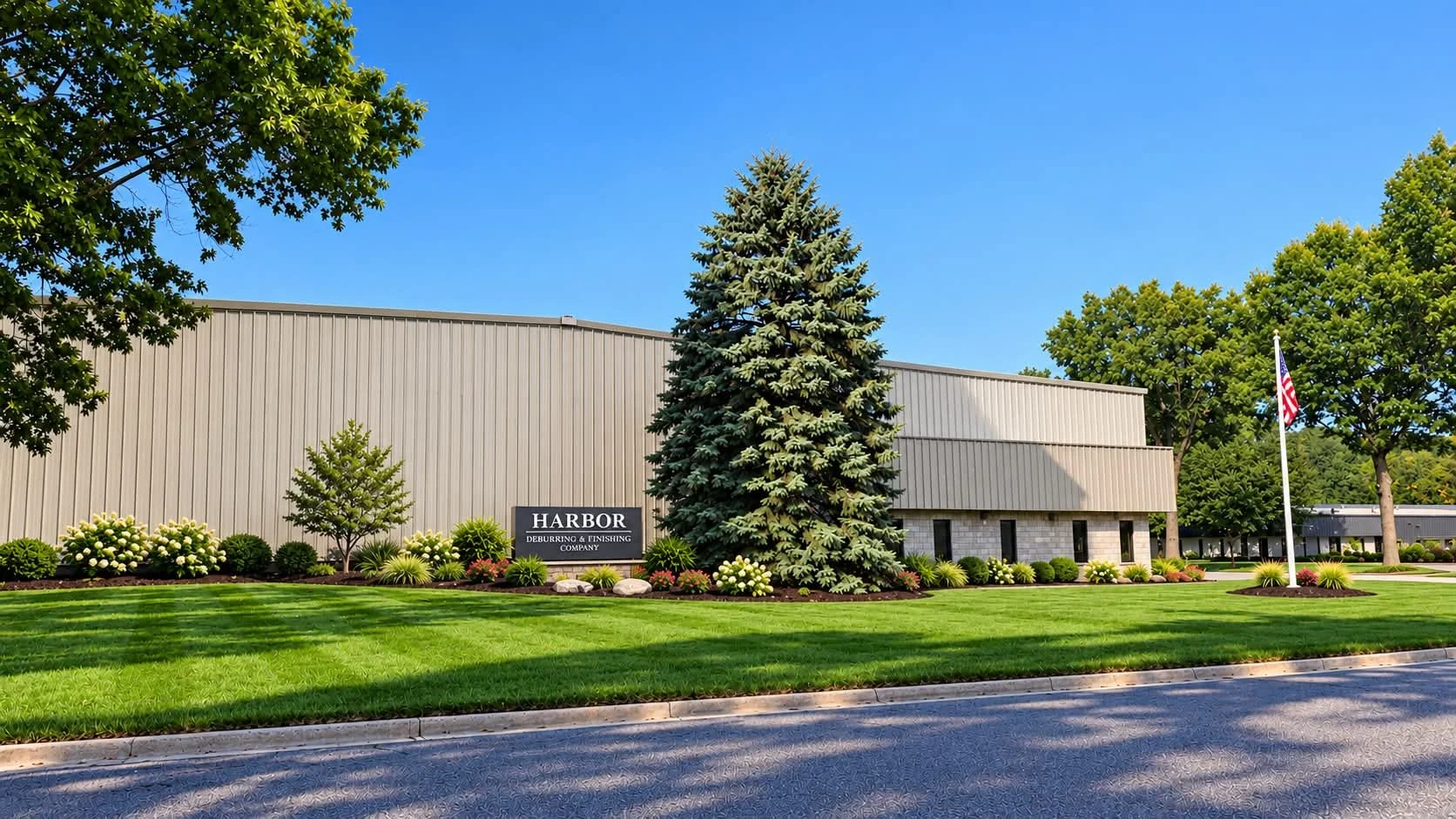 Harbor Deburring & Finishing Company industrial building with landscaped lawn, evergreen tree, and American flag