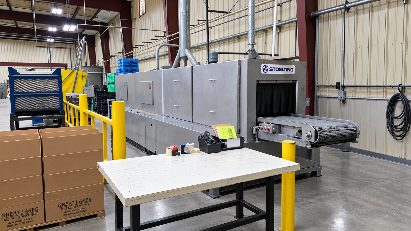 Industrial Stoelting conveyor machine in a metal stamping factory with cardboard shipping boxes and worktable