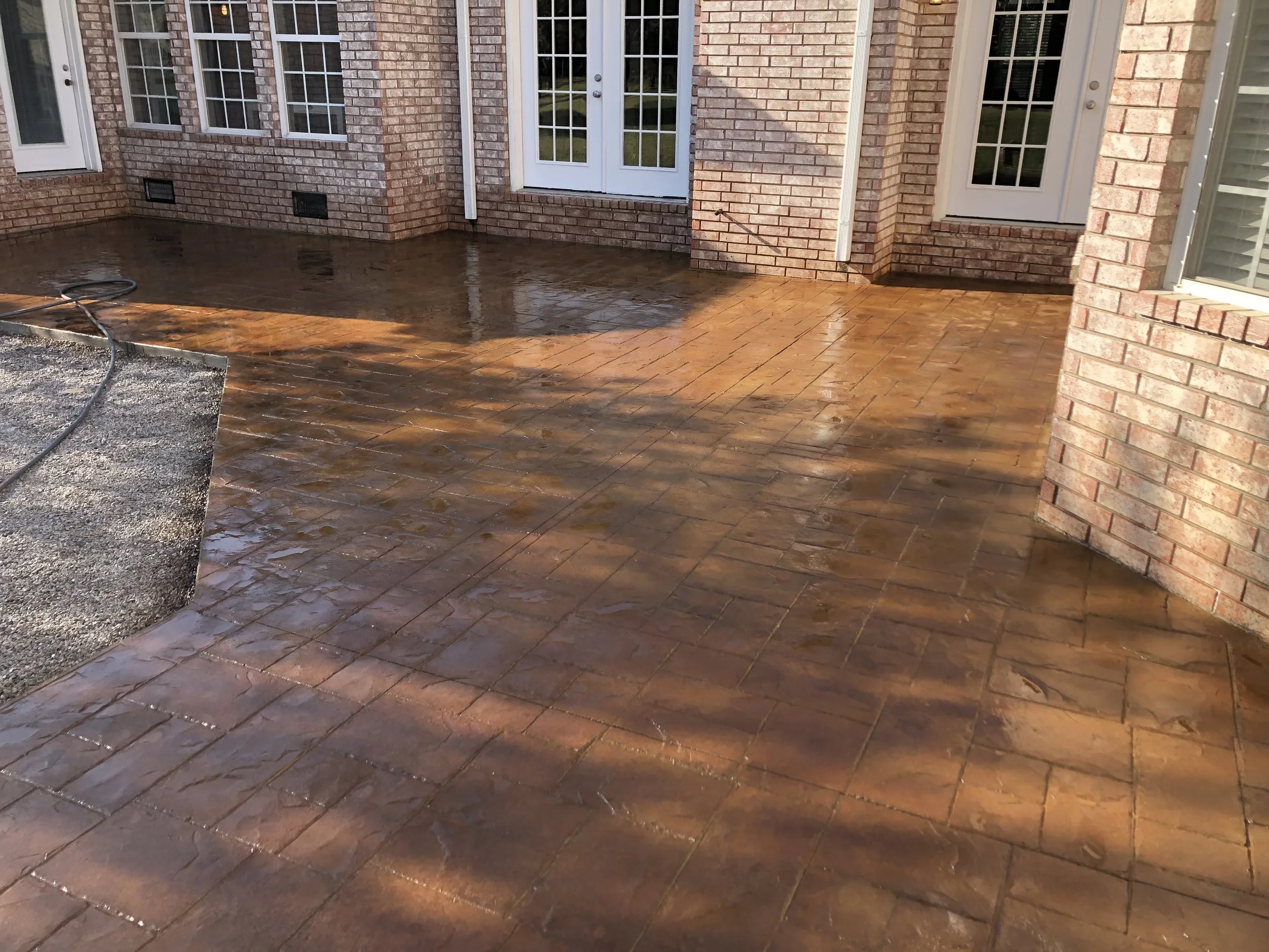 Backyard patio area with freshly cleaned brick patio flooring, white French doors, and brick exterior walls of a house.