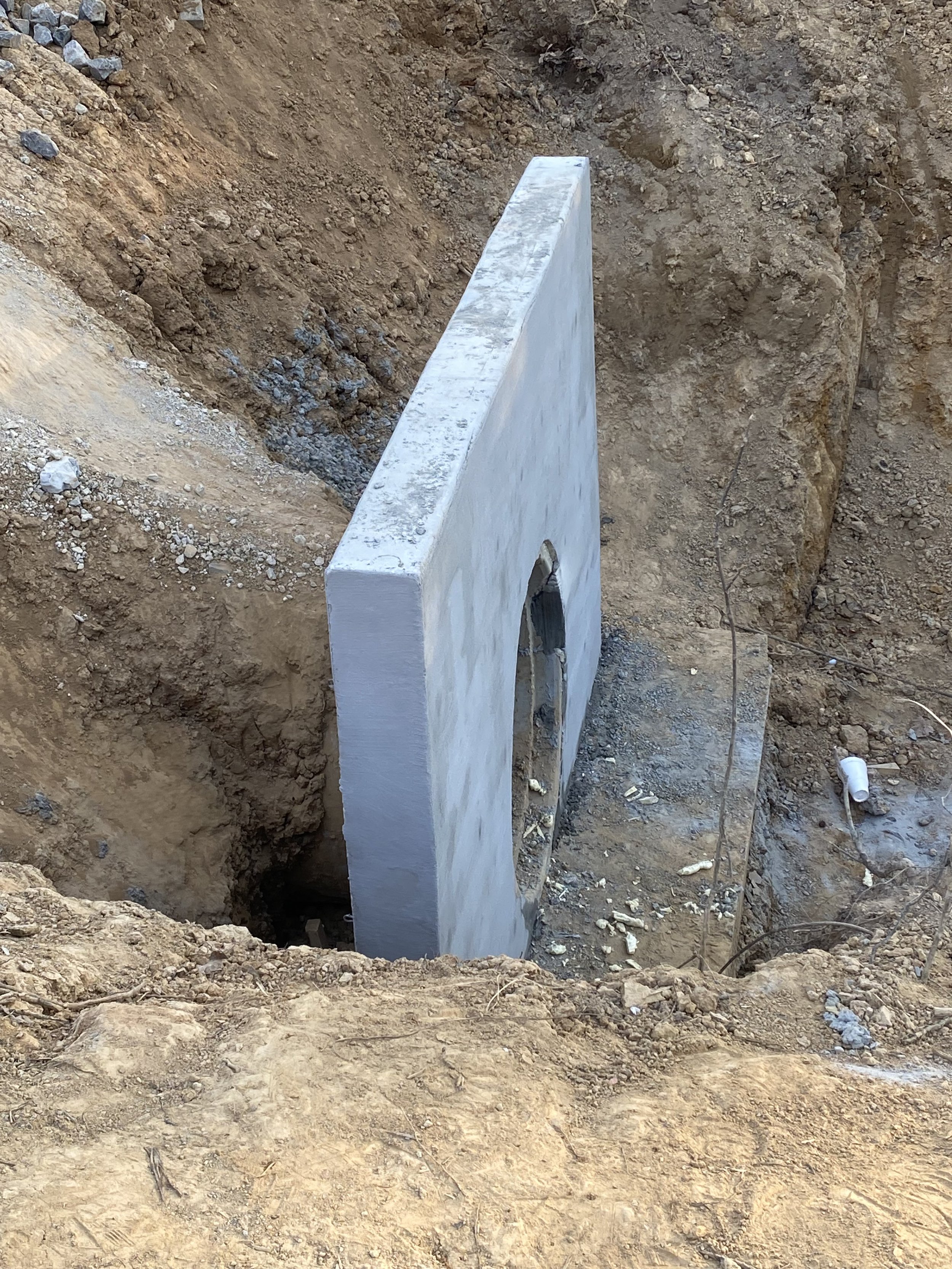 Concrete wall segment installed in a trench during construction, with dirt and soil surrounding it.