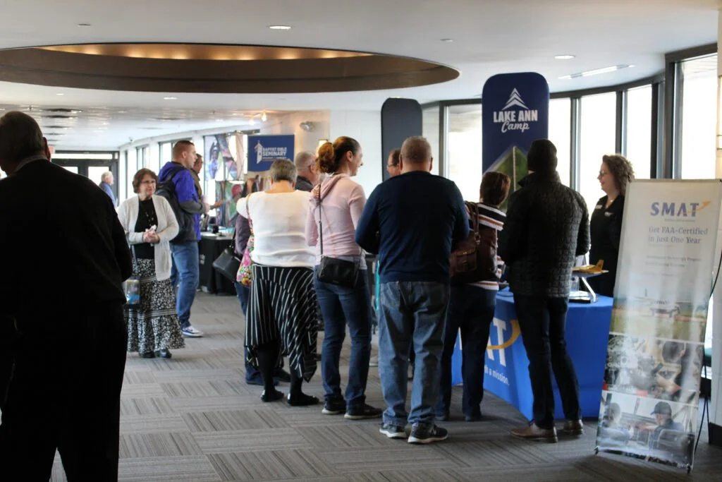 People attending a conference or expo in a large, modern hall with promotional booths and banners.
