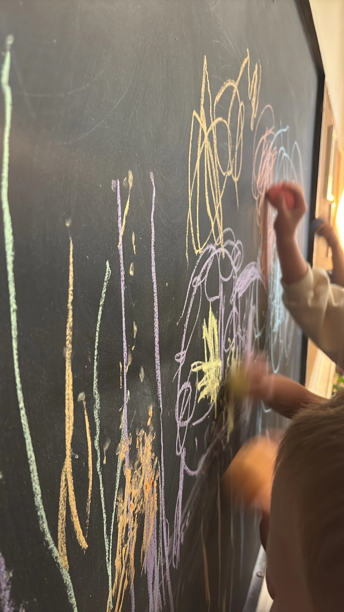 Children drawing colorful chalk art on a black chalkboard wall at Youngset Preschool.