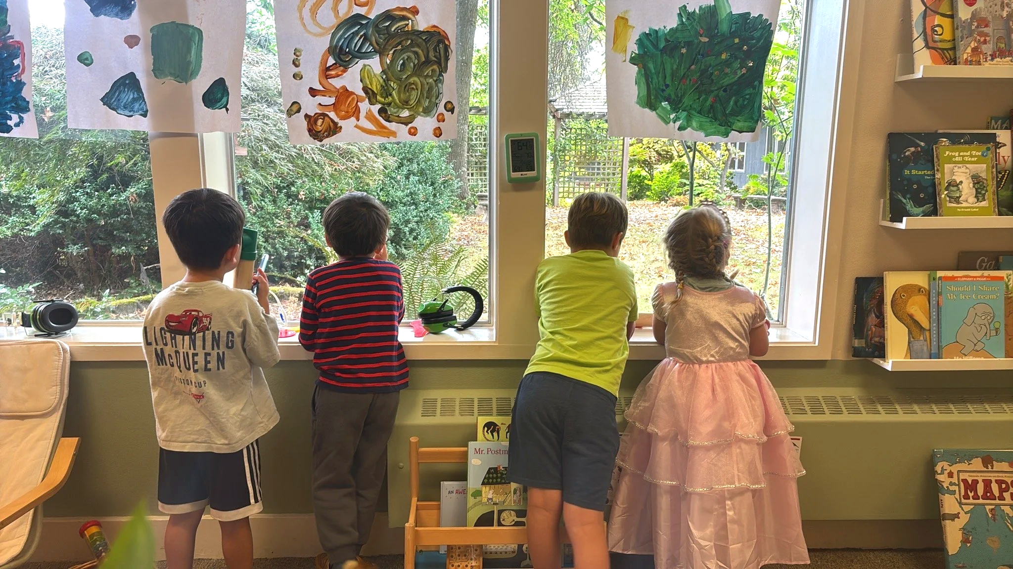 Five children at Youngset Preschool are standing in front of a large window, observing and pointing at trees outside.