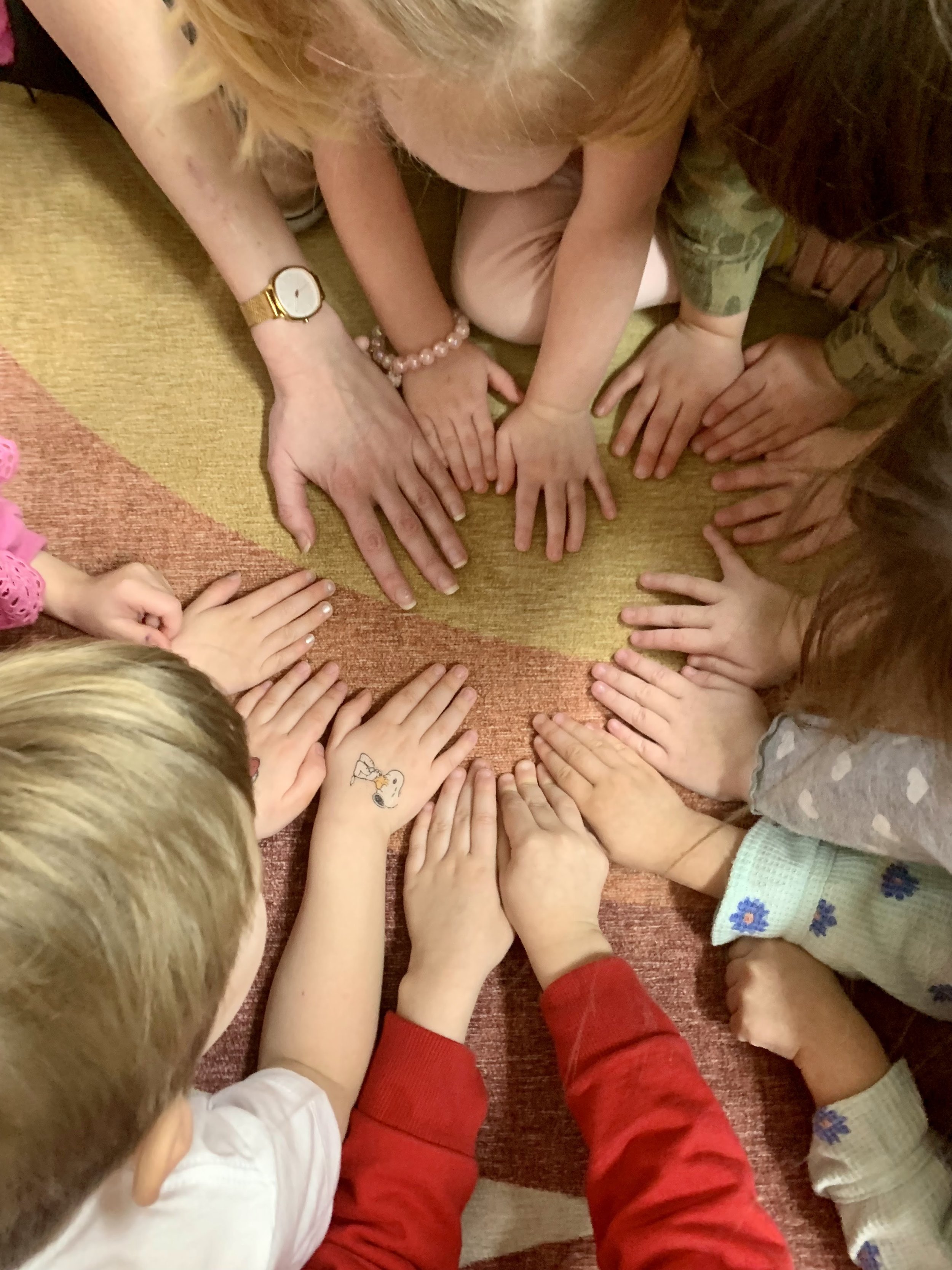 A group of children and adults at Youngset Preschool with their hands placed together on the floor, forming a circle for a shared activity.