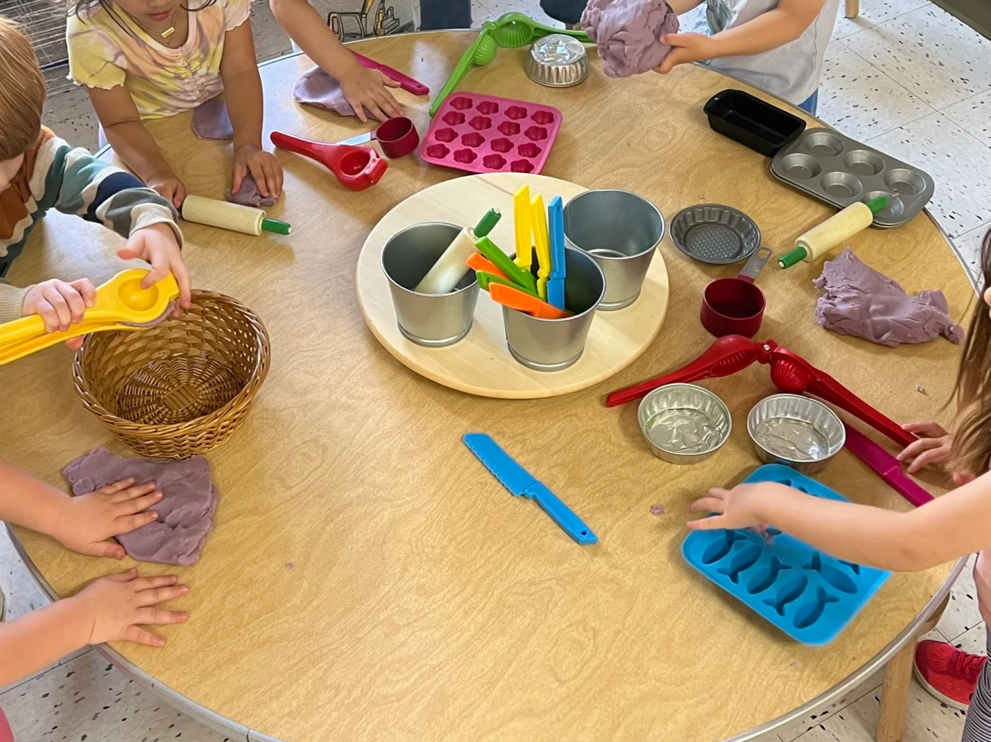 Children playing with colorful playdough and baking utensils at a round table at Youngset Preschool, engaging in imaginative cooking activities.