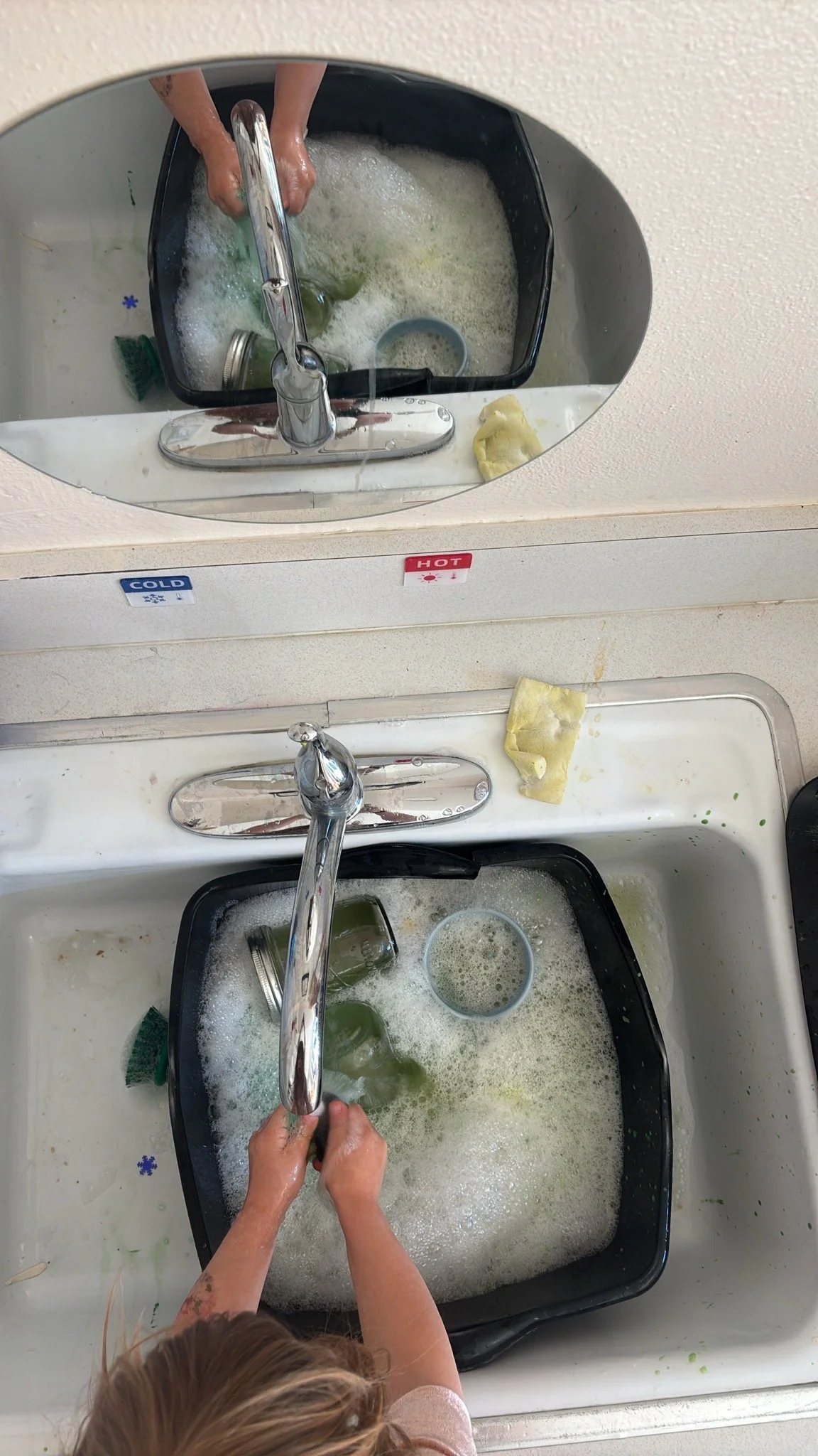 Child at Youngset Preschool washing dishes in a deep sink with foam and soap.