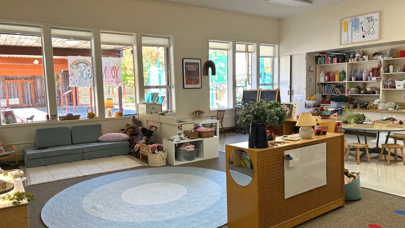 Bright and organized Youngset Preschool Juniors classroom with a blue sofa, children's artwork, toys, plants, and learning materials.