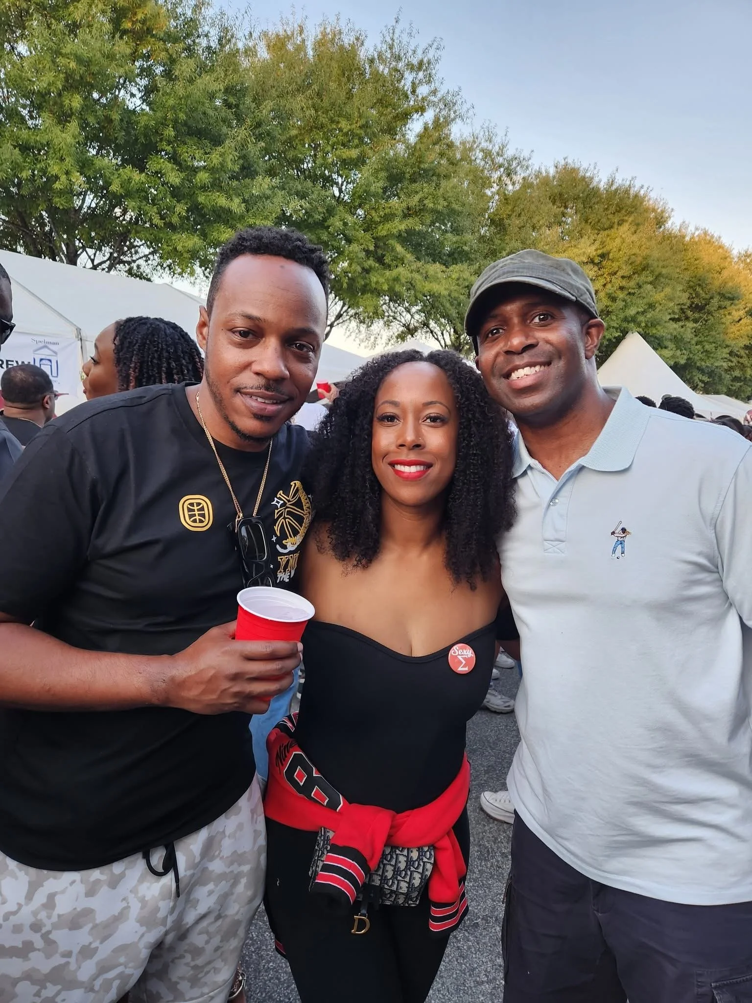 Three people smiling together at an outdoor community gathering.