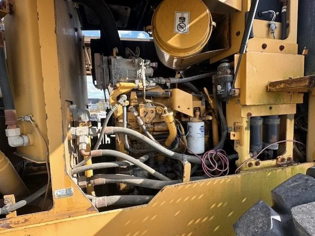 Close-up of a yellow construction or industrial machine showing hydraulic hoses, filters, and mechanical components.