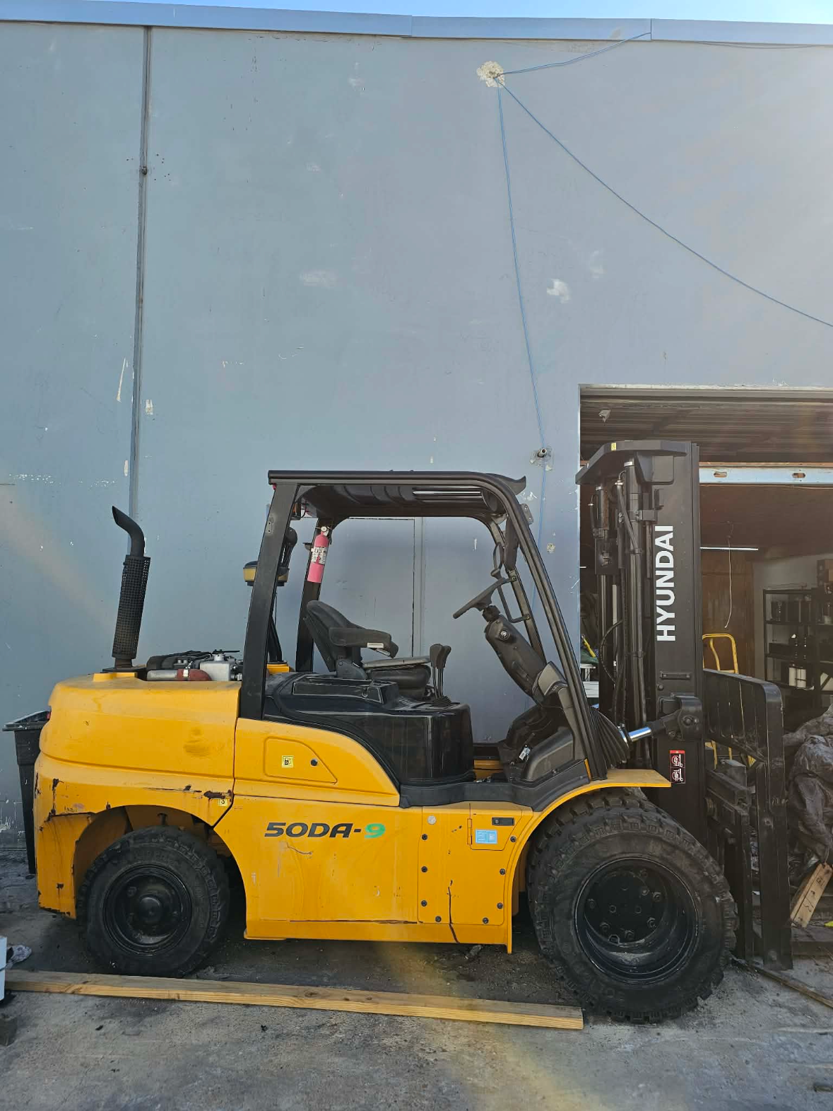 Yellow SODA-9 forklift parked outside a warehouse beside a black Hyundai forklift.