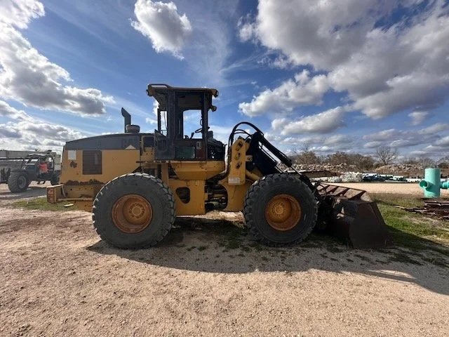 A yellow bulldozer parked on a gravel lot with a cloudy sky overhead.