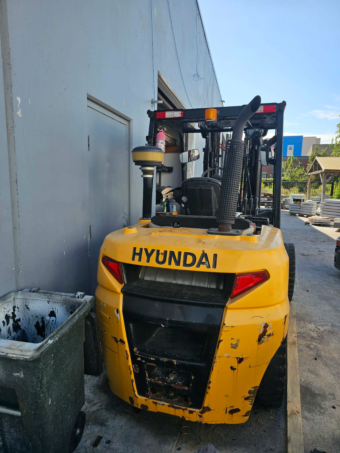 Rear view of a yellow Hyundai forklift parked beside an industrial building.