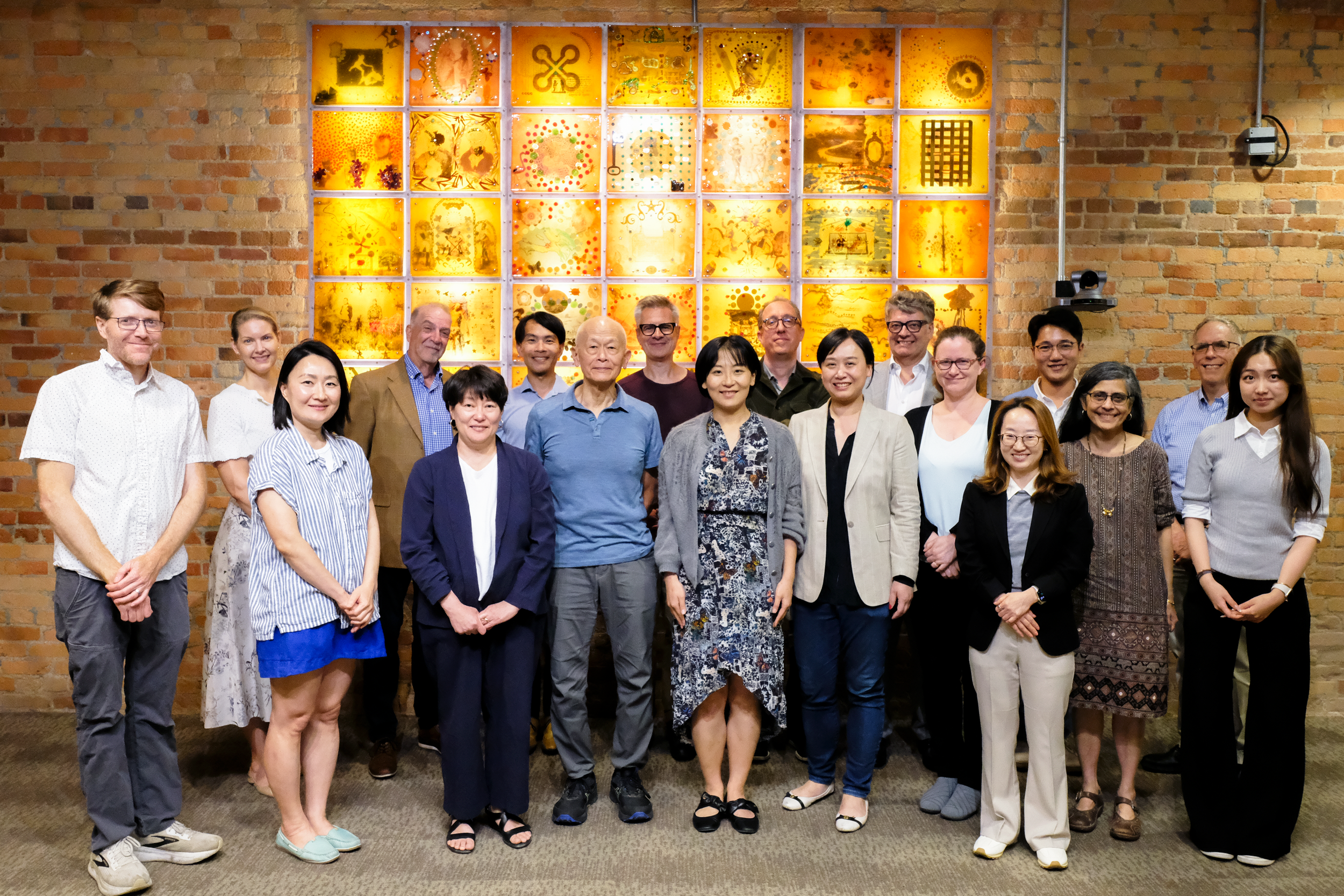 Group of diverse people standing together indoors in front of a brick wall with colorful illuminated art panels.