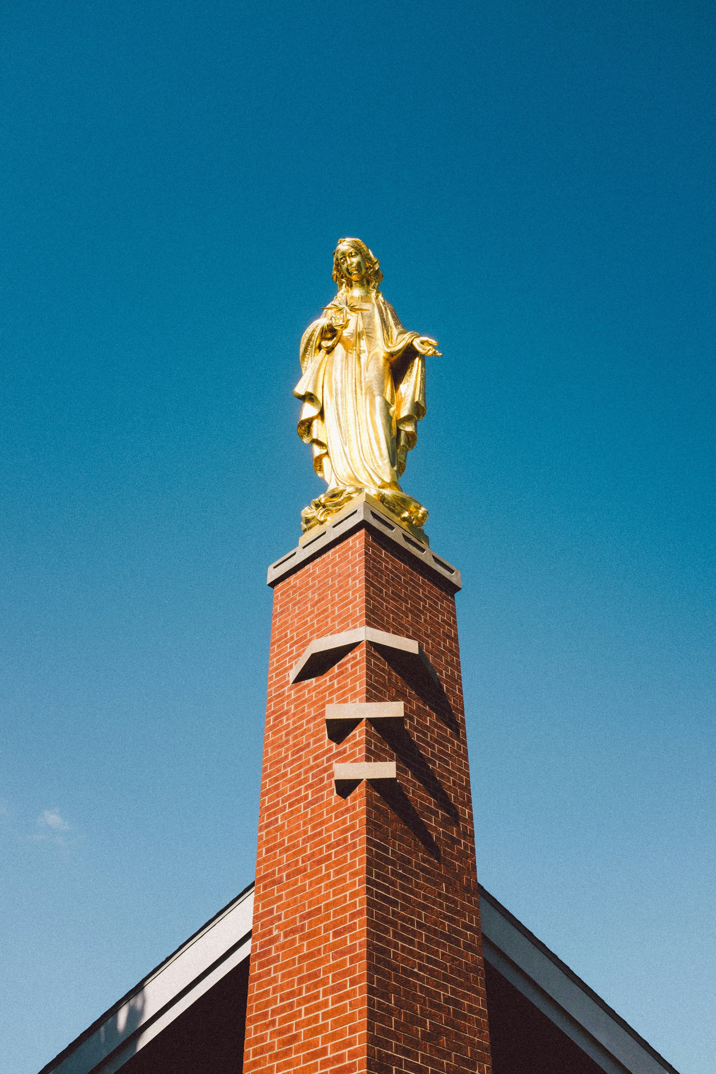 Gold statue of Jesus Christ on top of a red brick church steeple against a blue sky.