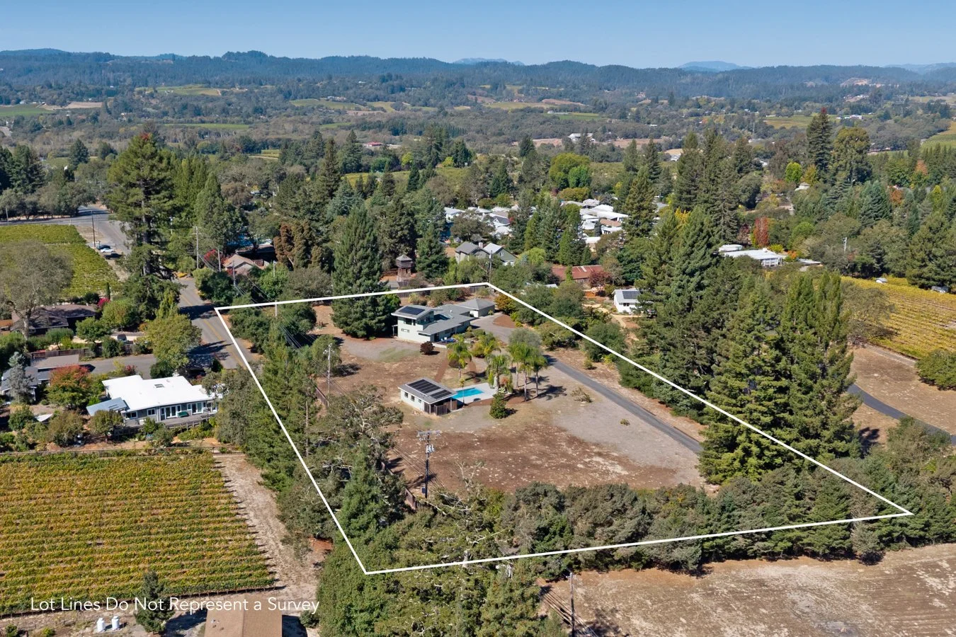 Aerial view of a suburban property with a house, a backyard pool, surrounded by trees and neighboring houses in a rural landscape.