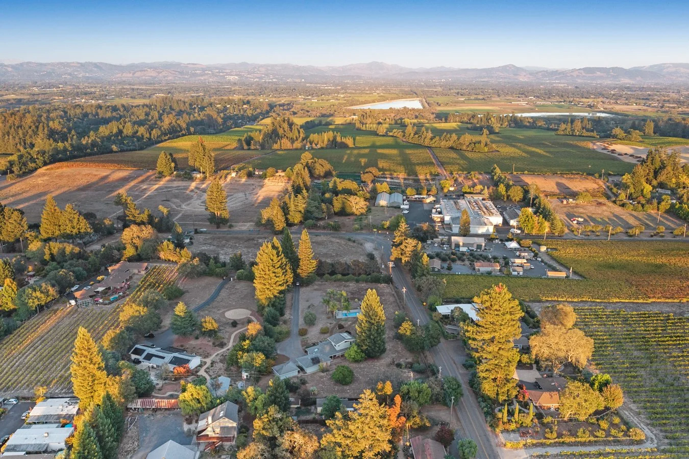 Aerial view of farmland with fields, trees, houses, and roads in a rural area during sunset.
