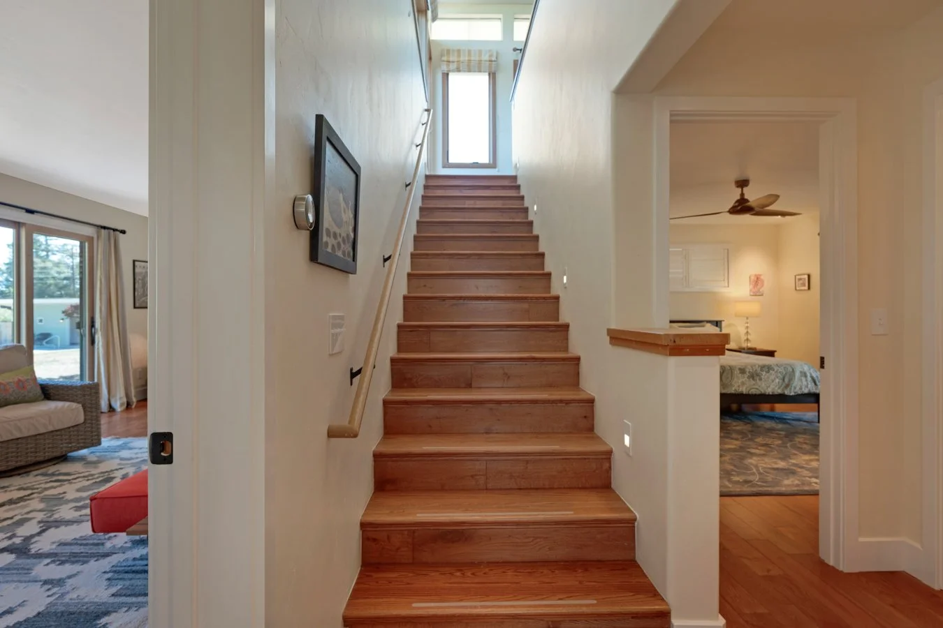 Wooden staircase leading up to a window at the top, with a sitting room on the left and a bedroom on the right.