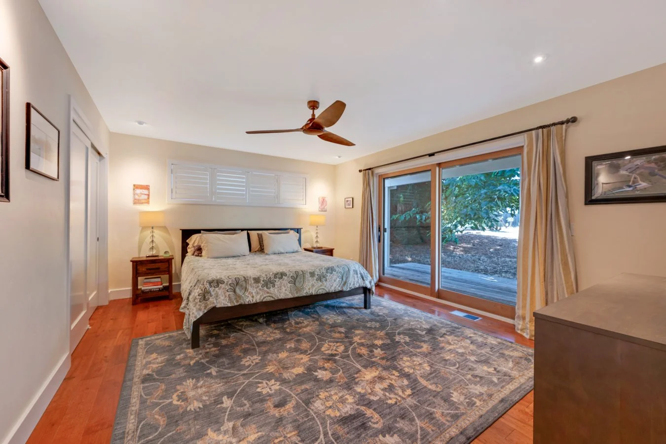 Bedroom with a bed, two nightstands with lamps, sliding glass door with curtains, and a ceiling fan.
