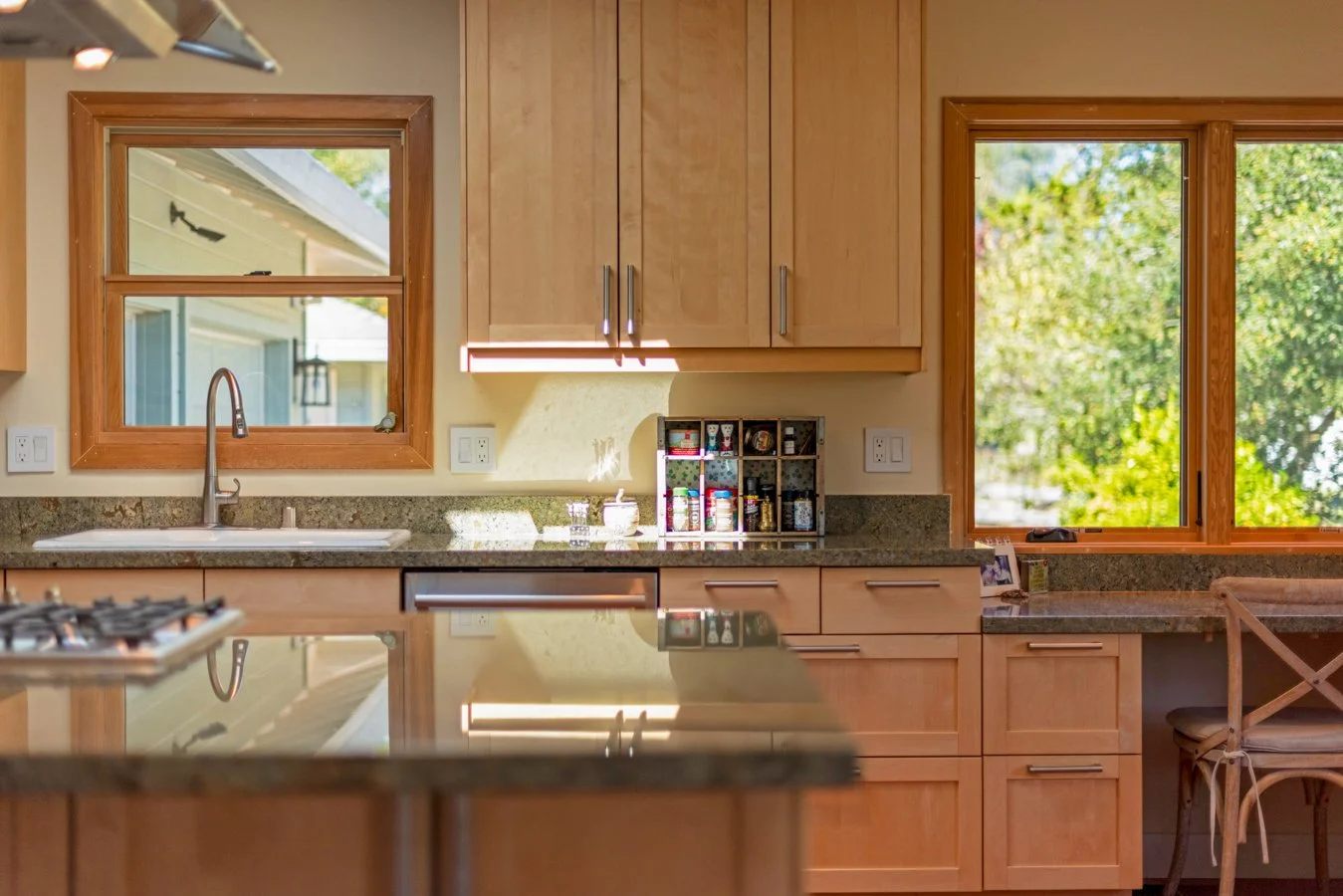 A kitchen with wooden cabinets, granite countertops, a double window above the sink, and a sliding door with a view of trees outside.