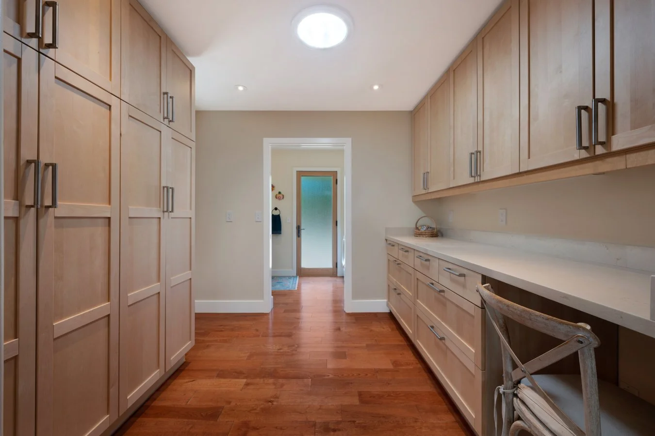 A kitchen with wooden cabinets, white countertops, hardwood floors, and a door leading outside.