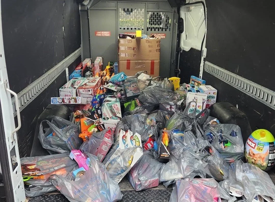 Inside of a delivery truck filled with garbage bags and boxes of toys and household items