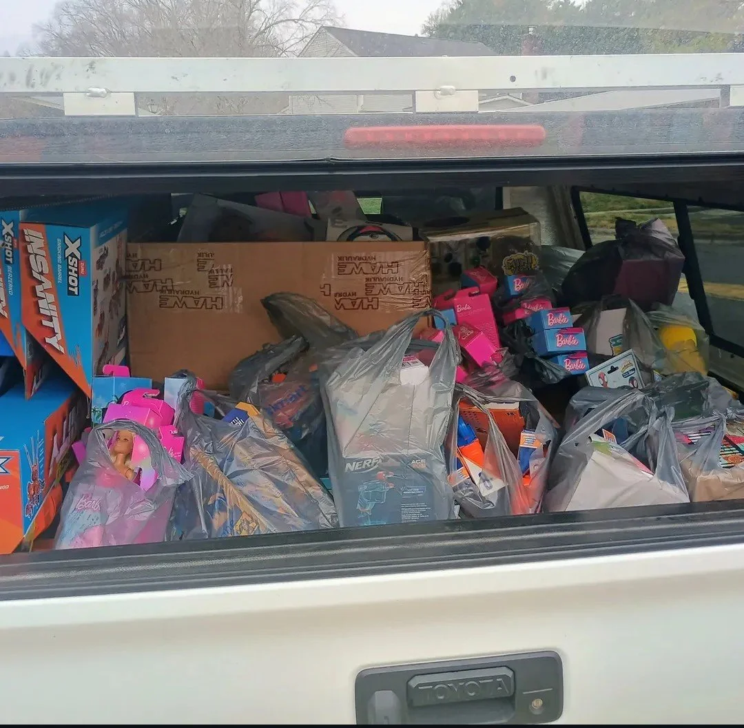 The back of a vehicle filled with plastic bags and boxes containing toys and games.