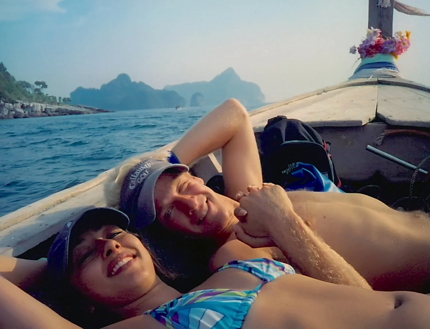 Two people relaxing on a boat with scenic mountains and ocean in the background, smiling and enjoying their time.